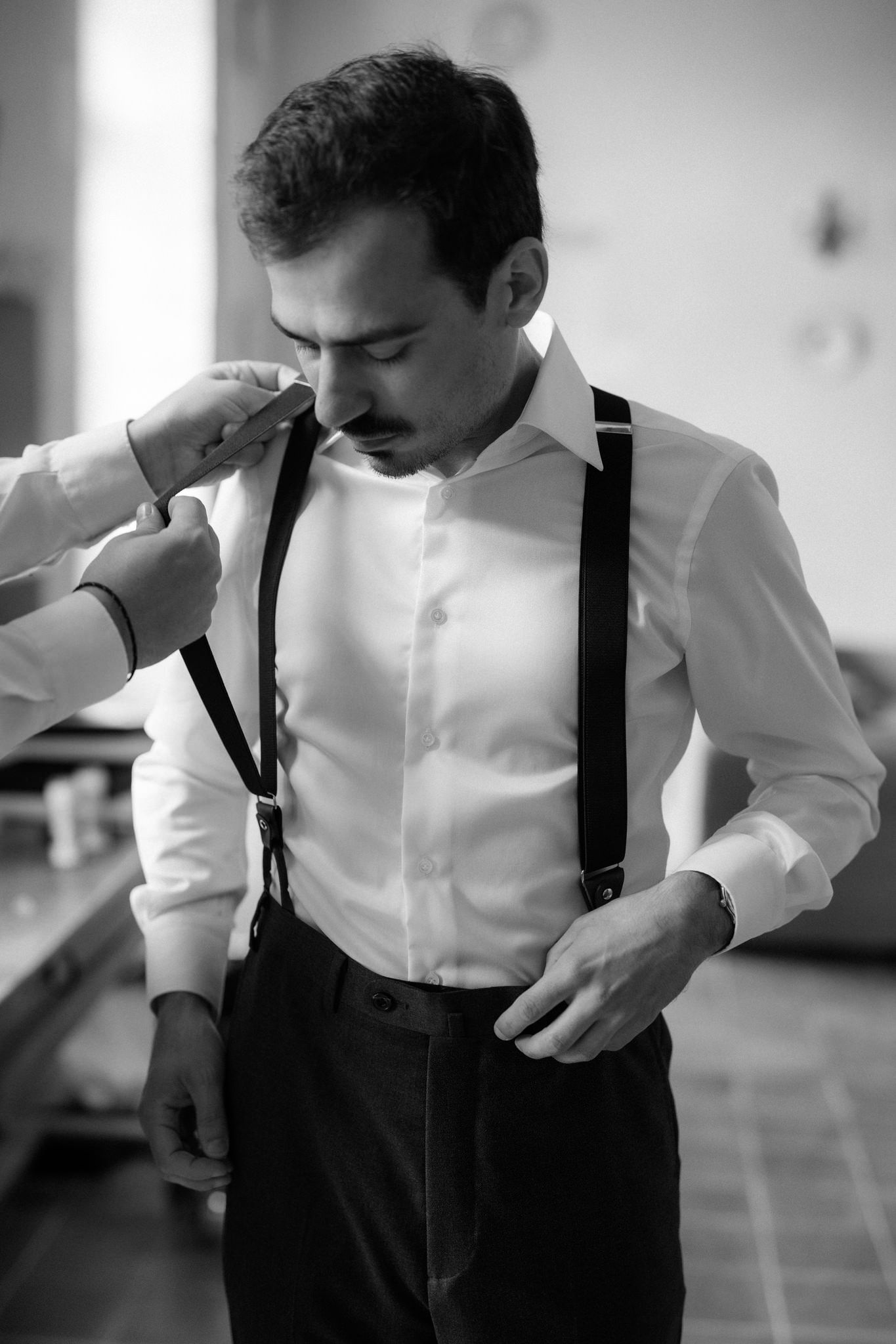 Person in formal attire with black suspenders getting dressed.