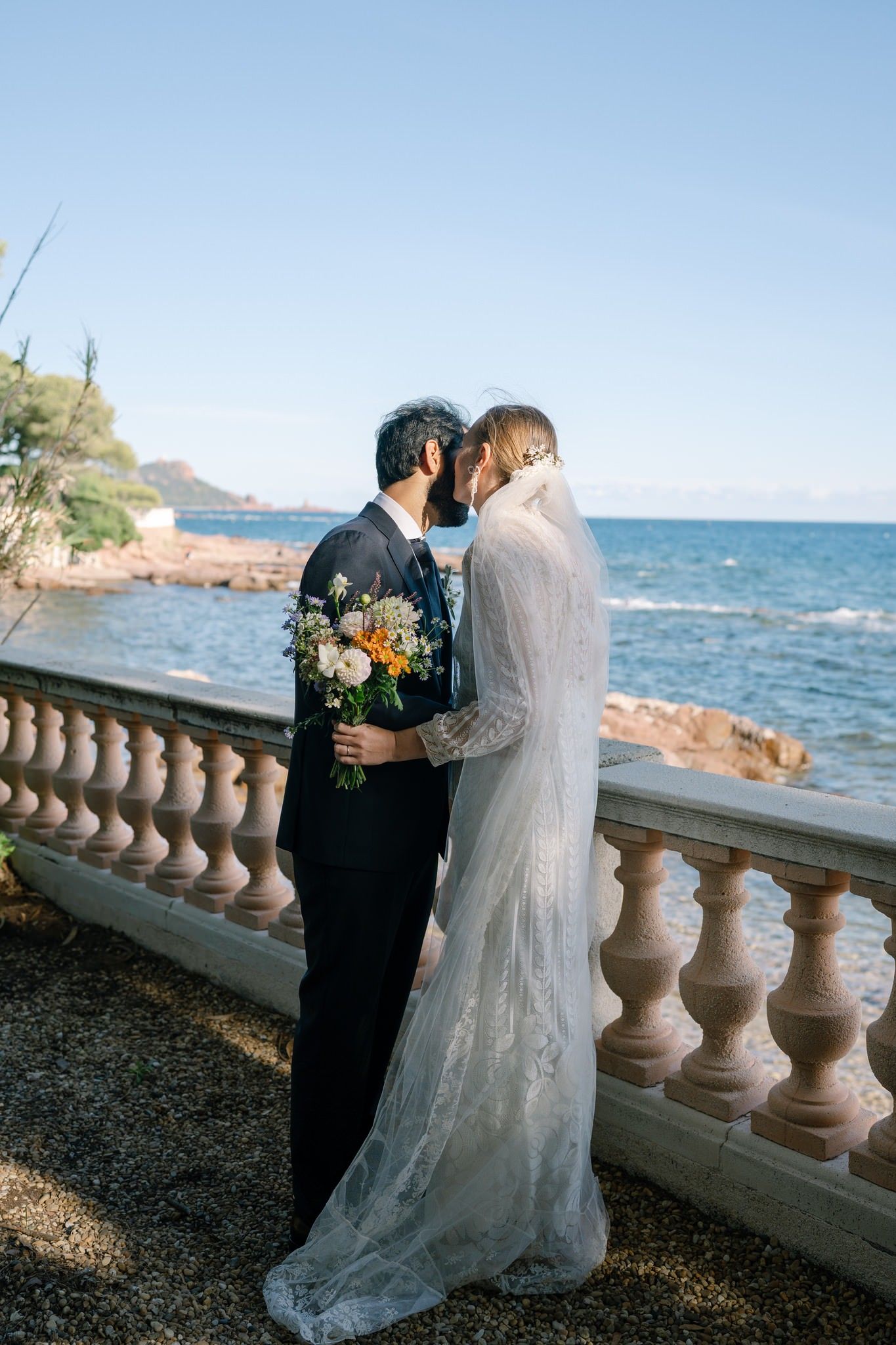 Couple shares intimate moment by stone balustrade overlooking ocean on their wedding day.