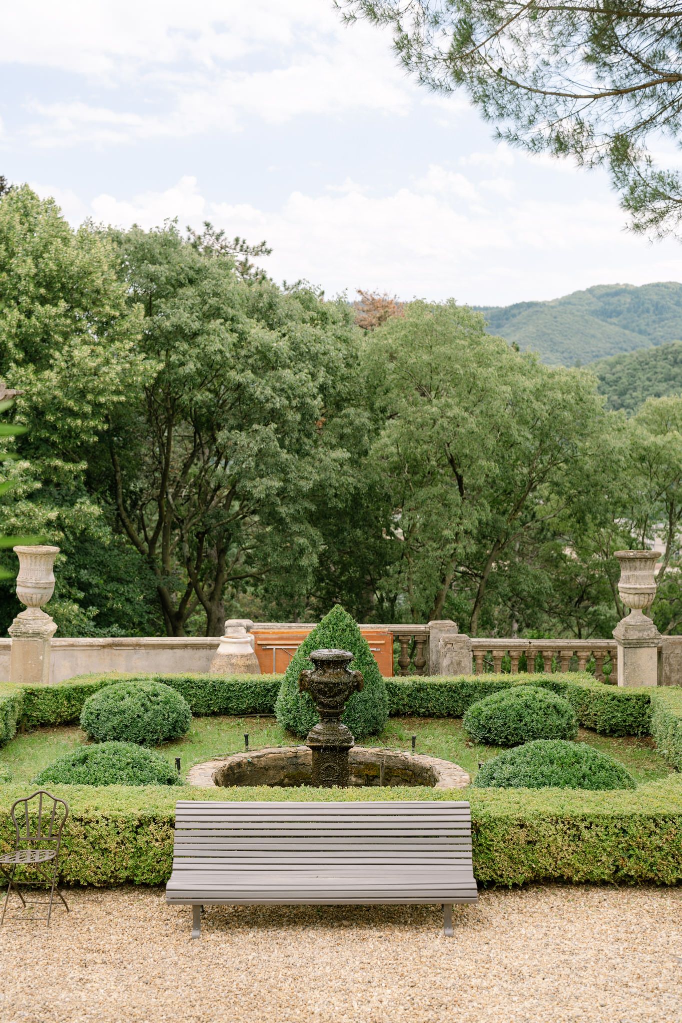 Elegant garden terrace with stone benches and manicured hedges overlooking mountains.
