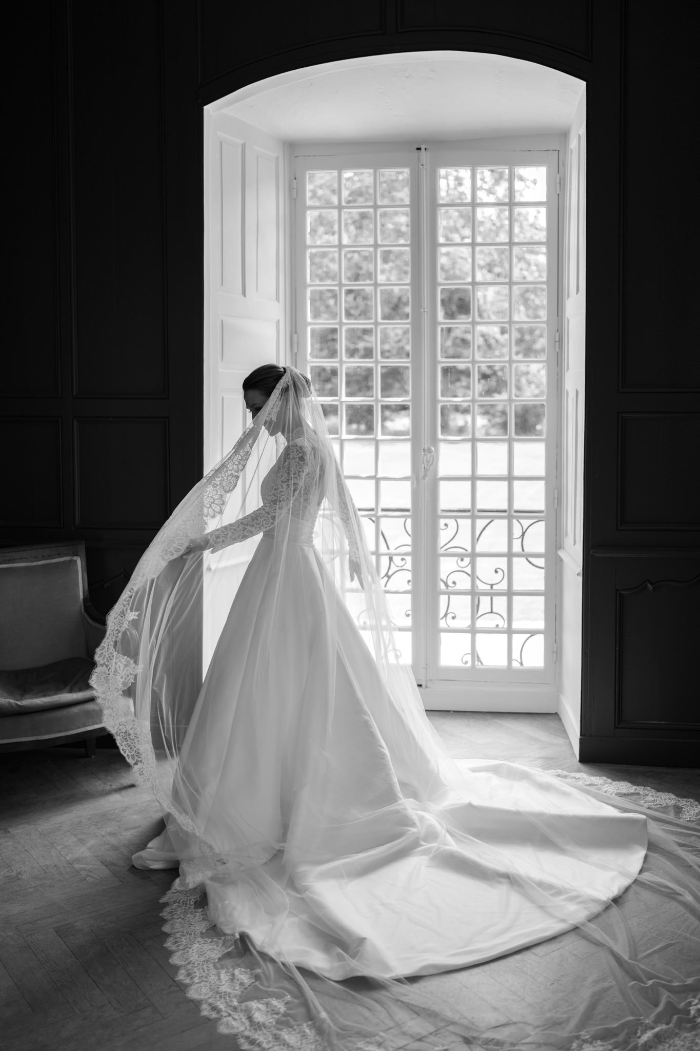 Dramatic black and white photos of flowing wedding dress near bright window.