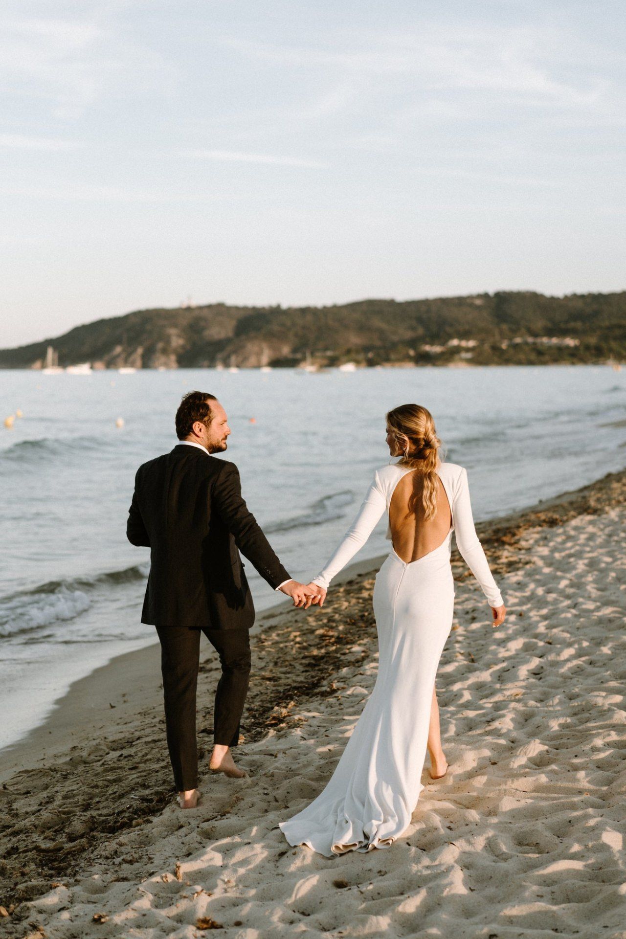 Couple walking hand in hand along a scenic beach at sunset.