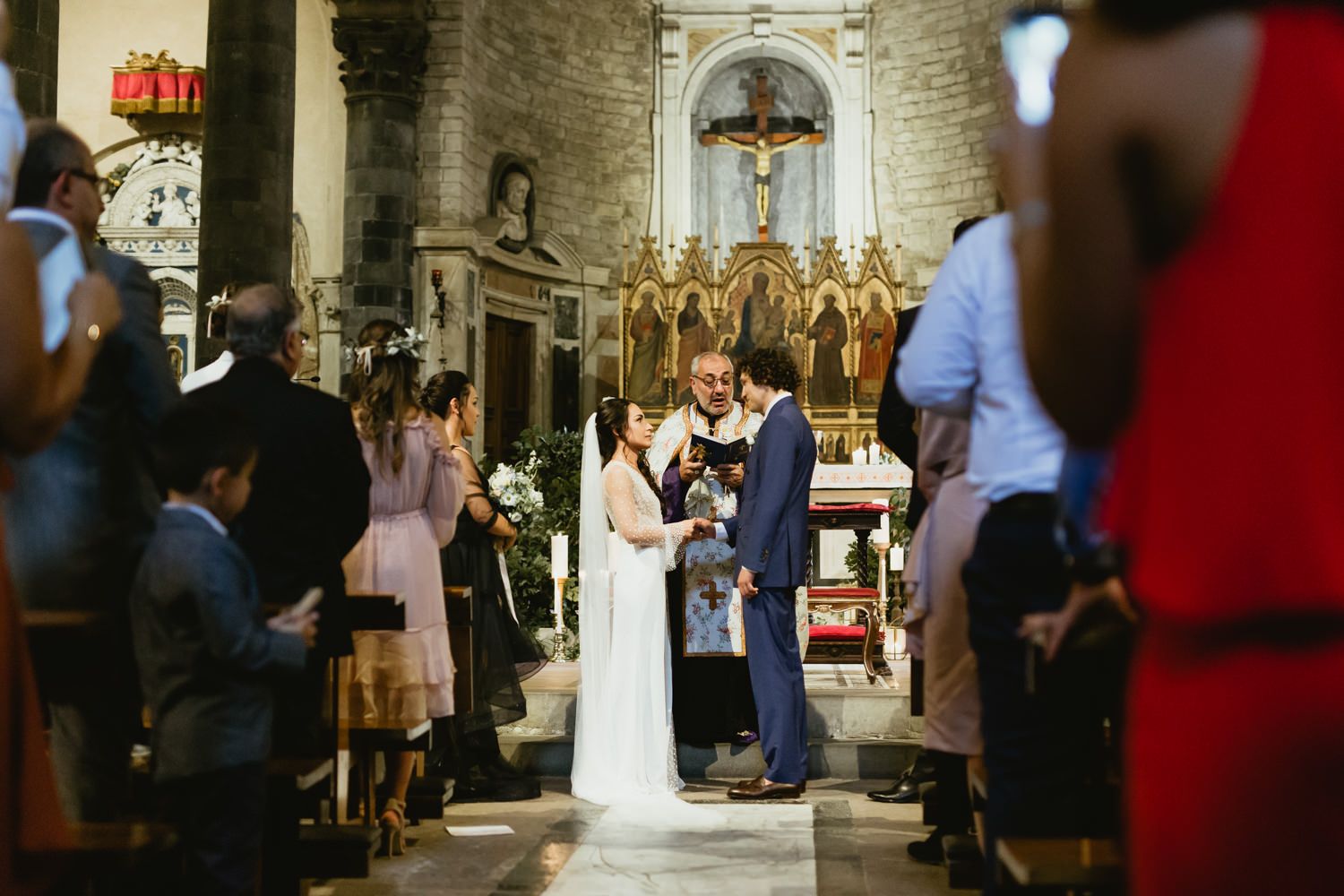 Wedding ceremony taking place at ornate church altar with guests watching from wooden pews.