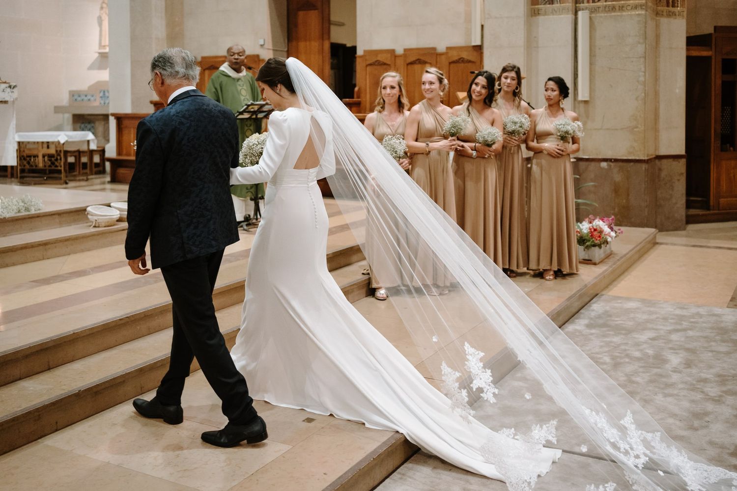 Wedding ceremony in traditional church with flowing white veil and bridesmaids in champagne dresses.