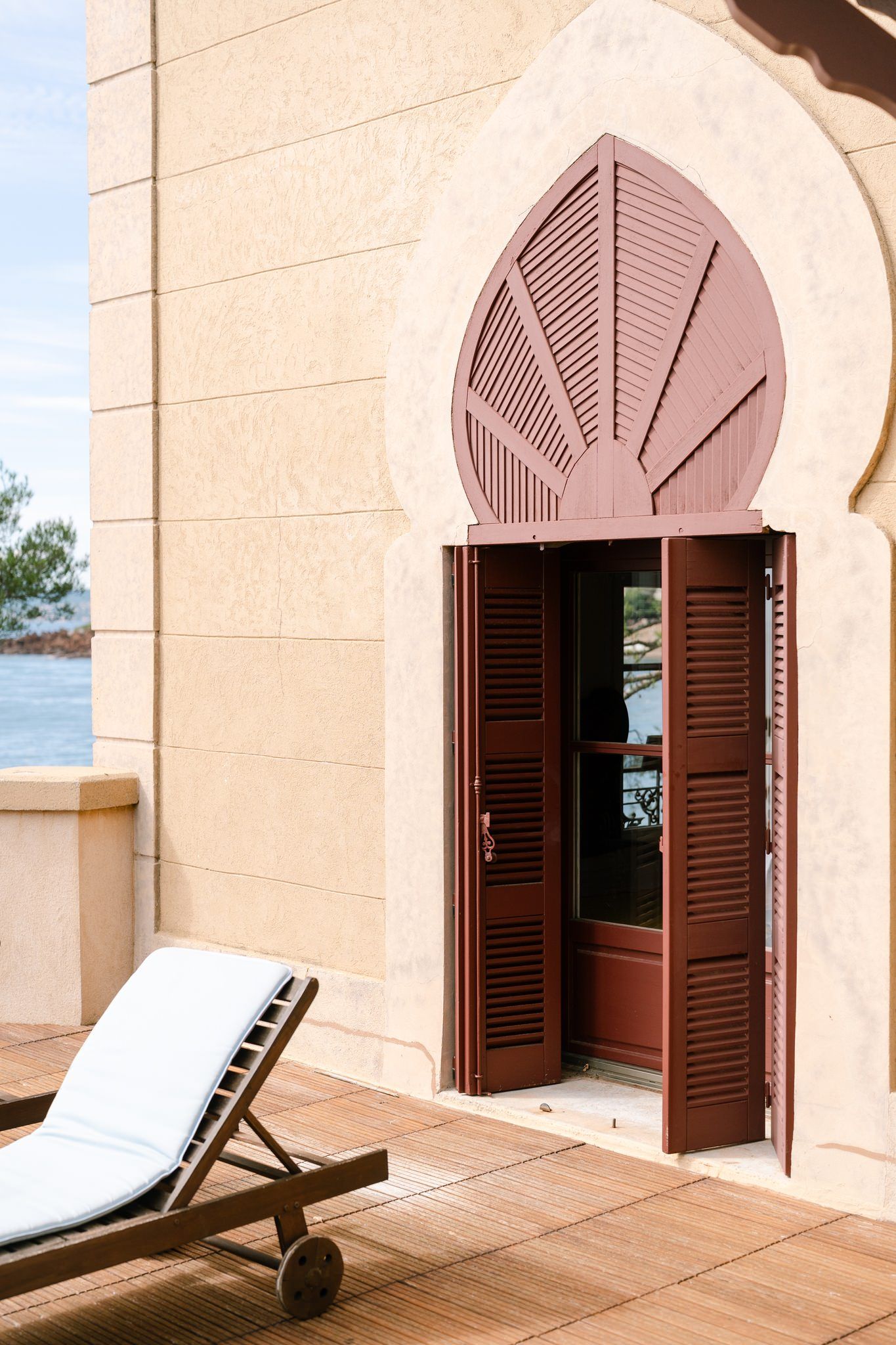 Arched doorways with wooden shutters and a lounge chair on a Mediterranean terrace.