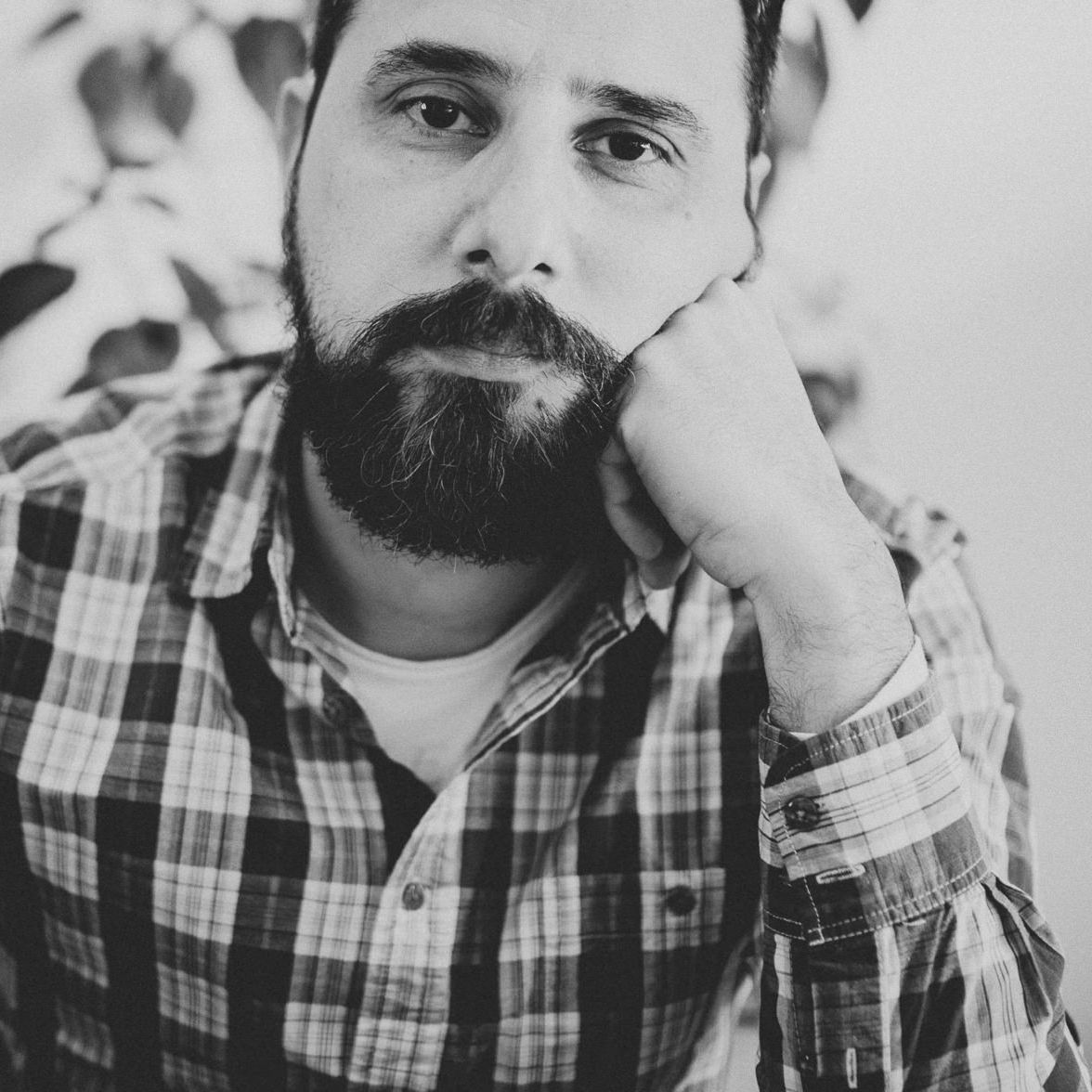 Monochrome headshot of someone in casual plaid shirt resting head on hand with thoughtful expression.