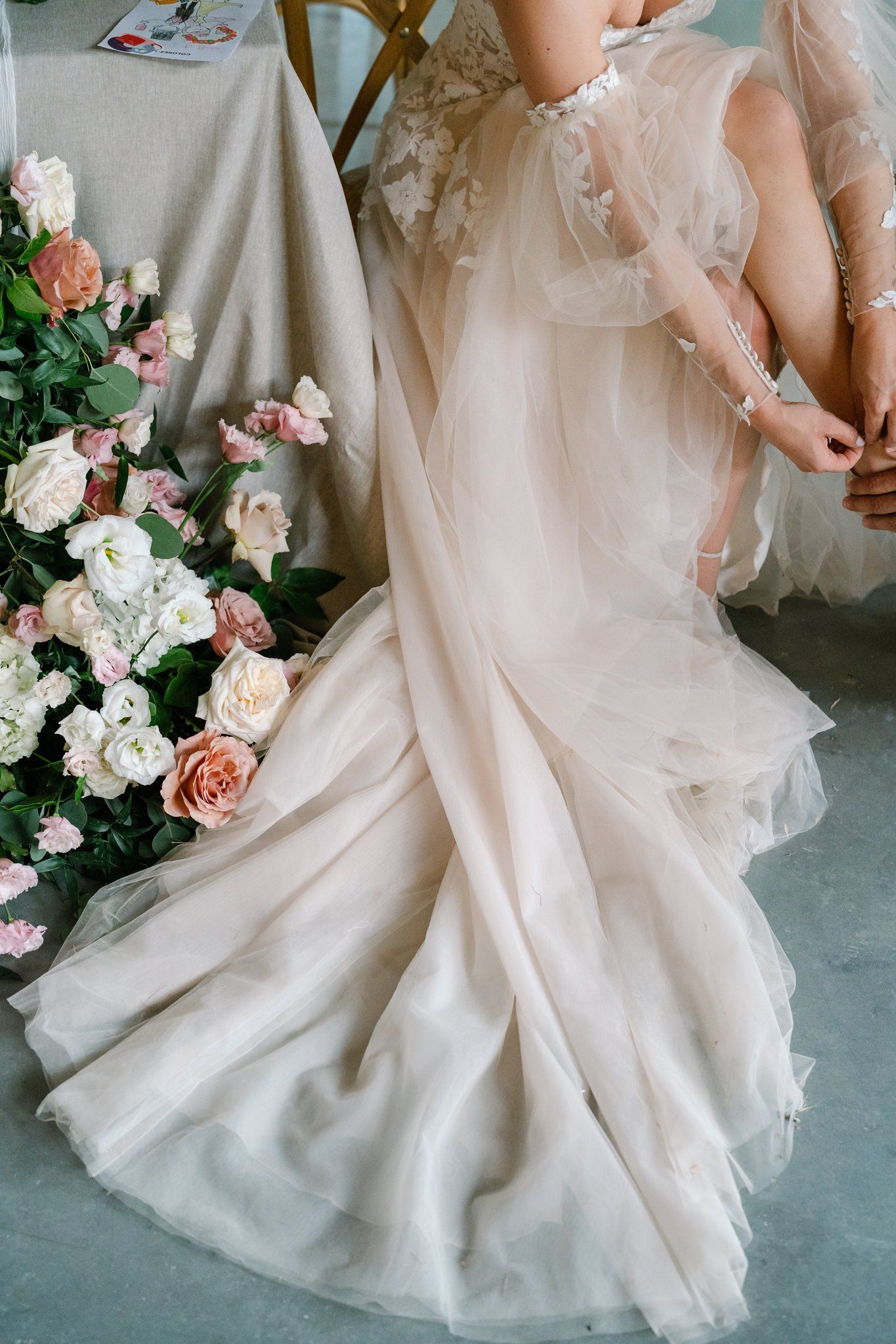 Close-up details of a flowing white wedding dress with delicate floral arrangements in pink and white.