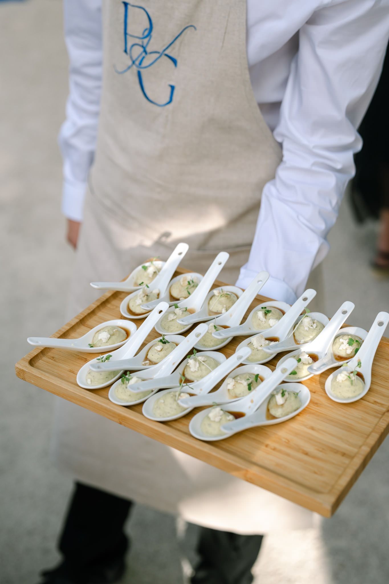 Elegant appetizer spoons arranged on a wooden serving board at a catered event.