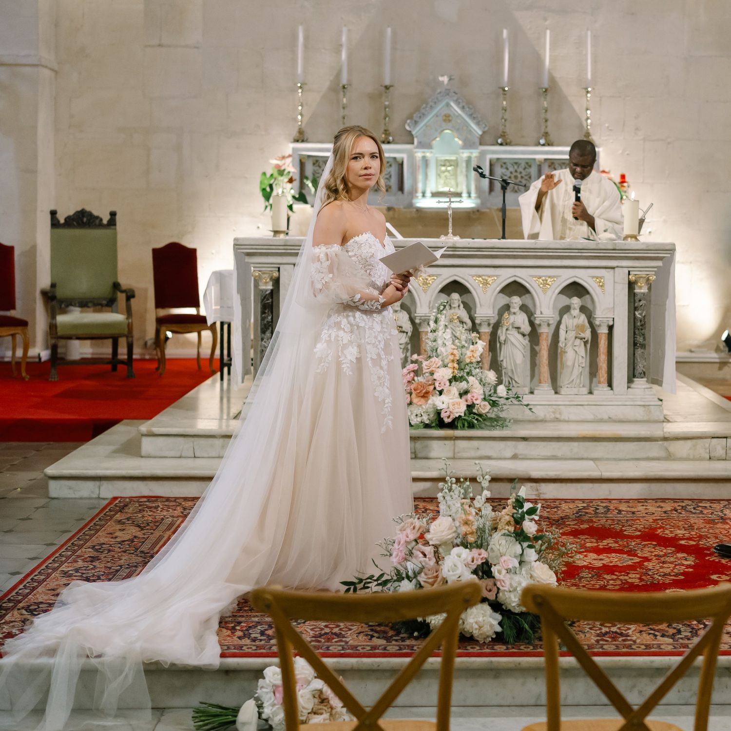 Wedding ceremony at church altar with white floral decorations and red carpet.