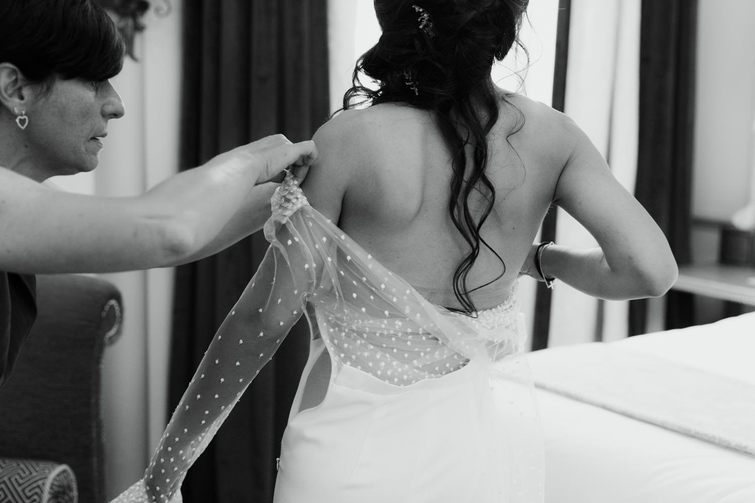 Behind the scenes black and white photo of a bride getting help with her wedding dress.