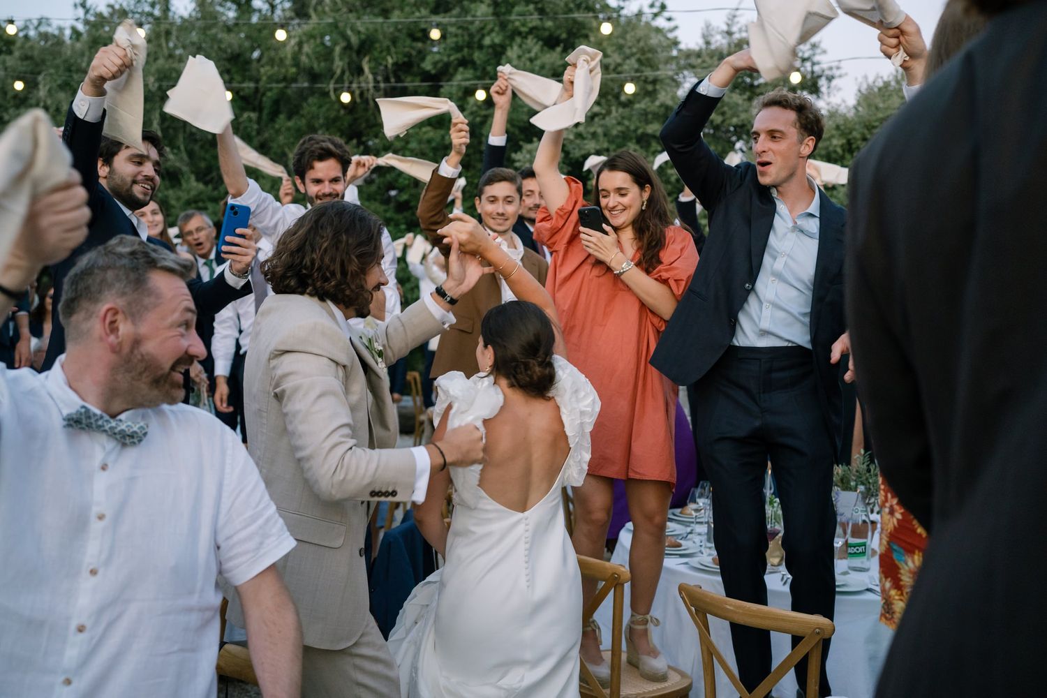 Energetic wedding celebration with guests dancing and waving napkins in the air.