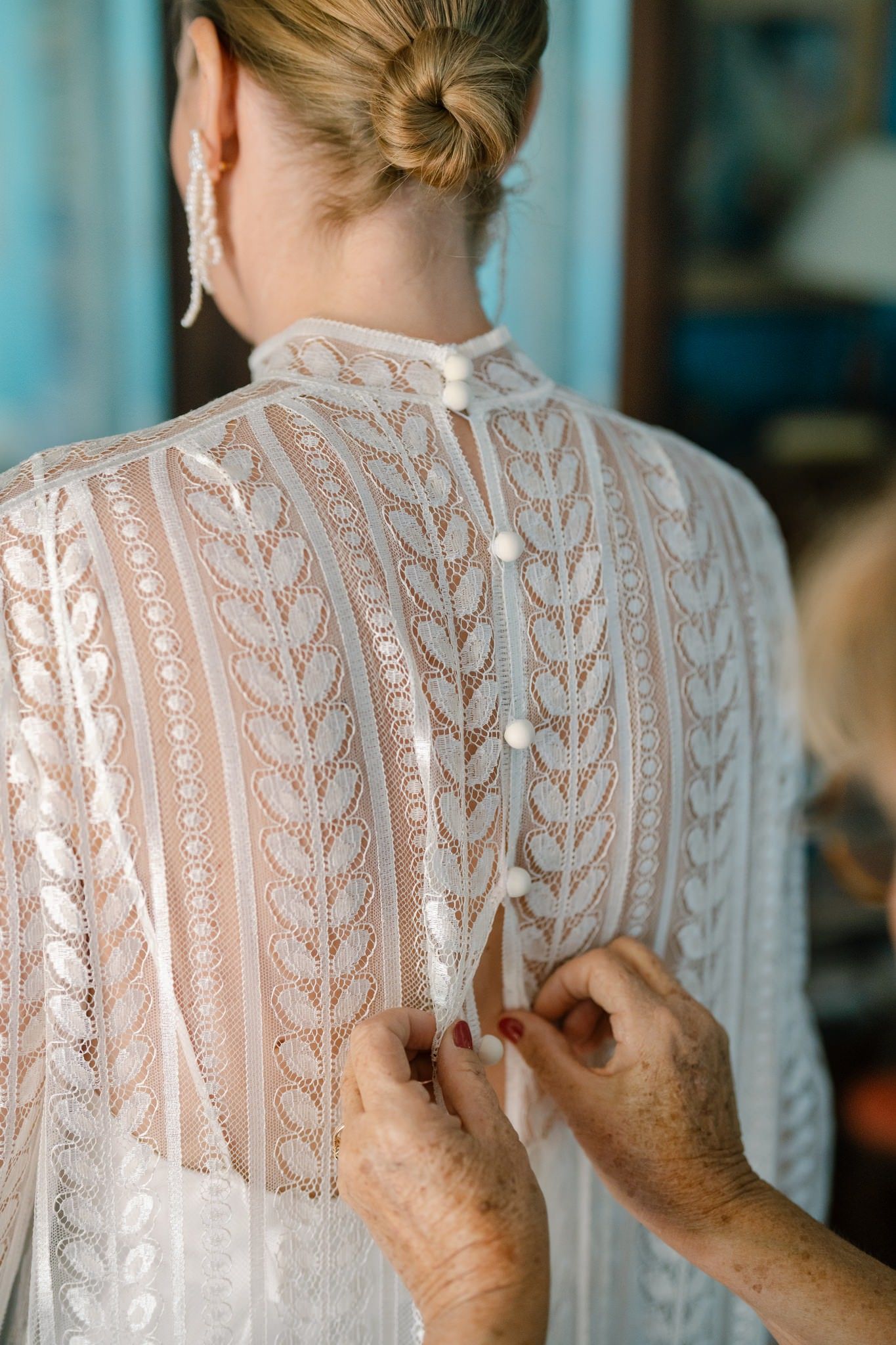 Detailed back view of an intricate white lace wedding dress being buttoned.
