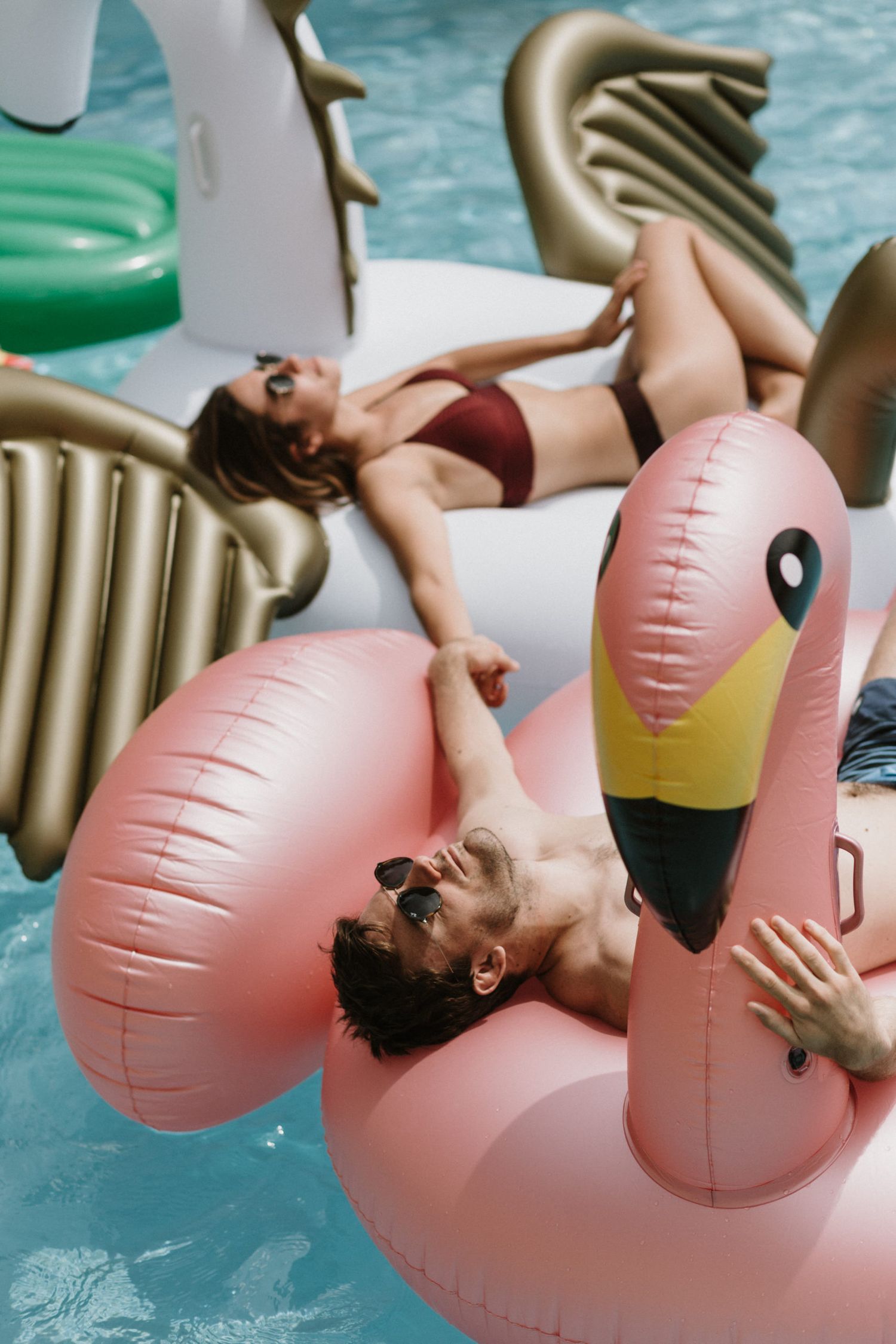 Person relaxing on a pink flamingo pool float in blue water.