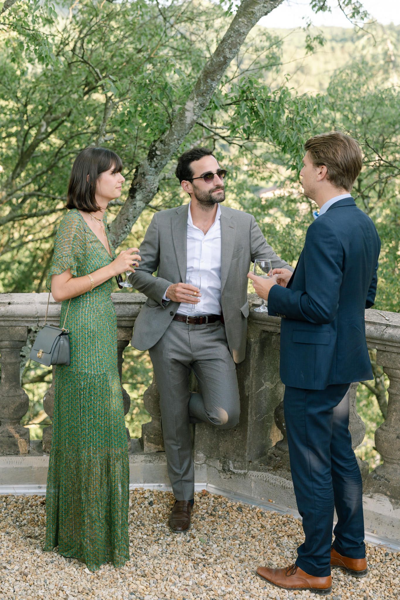 Wedding guests chat and mingle on a stone terrace during cocktail hour.