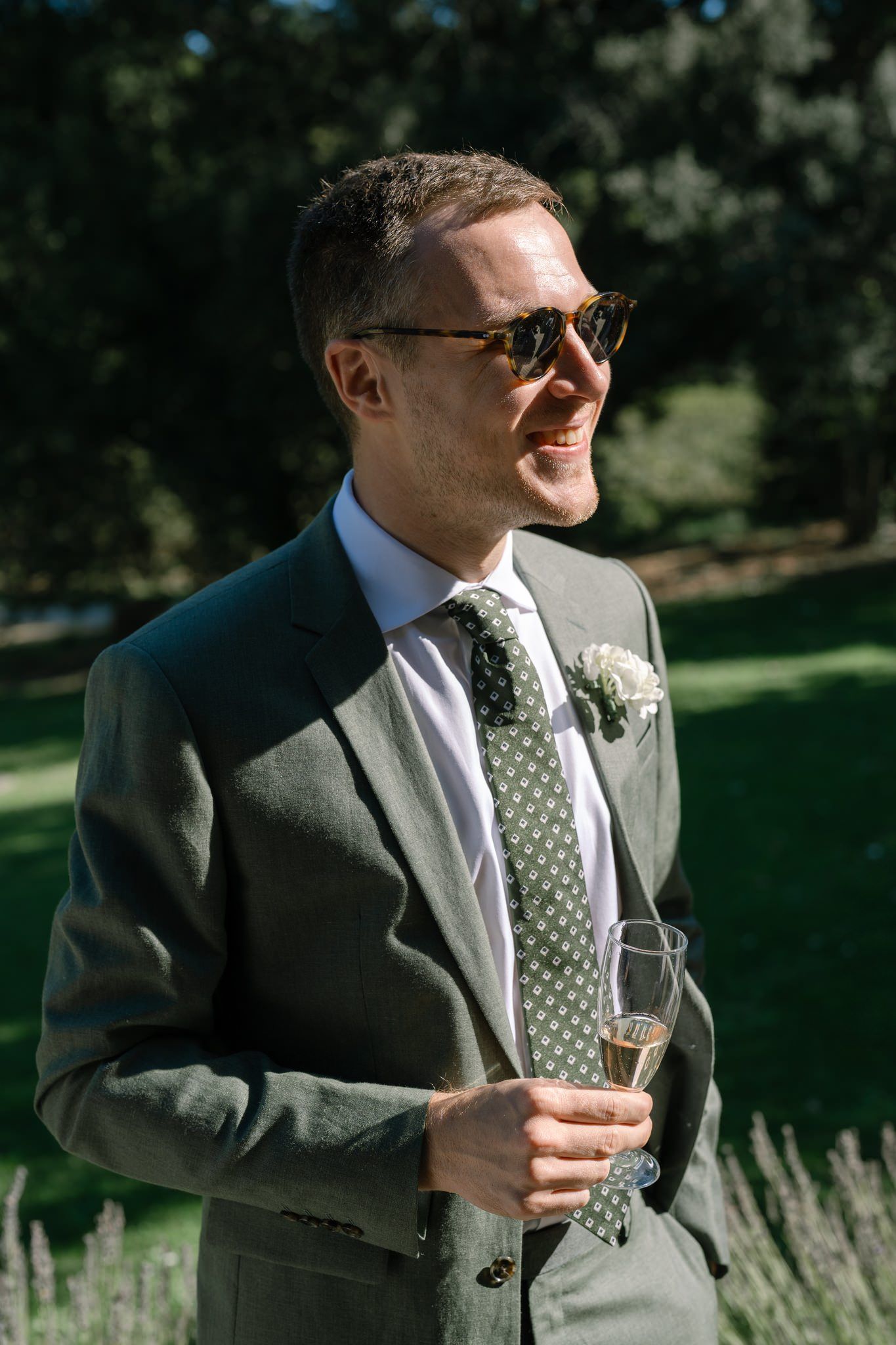 Groomsmen in grey suits and polka dot ties enjoying drinks outdoors.