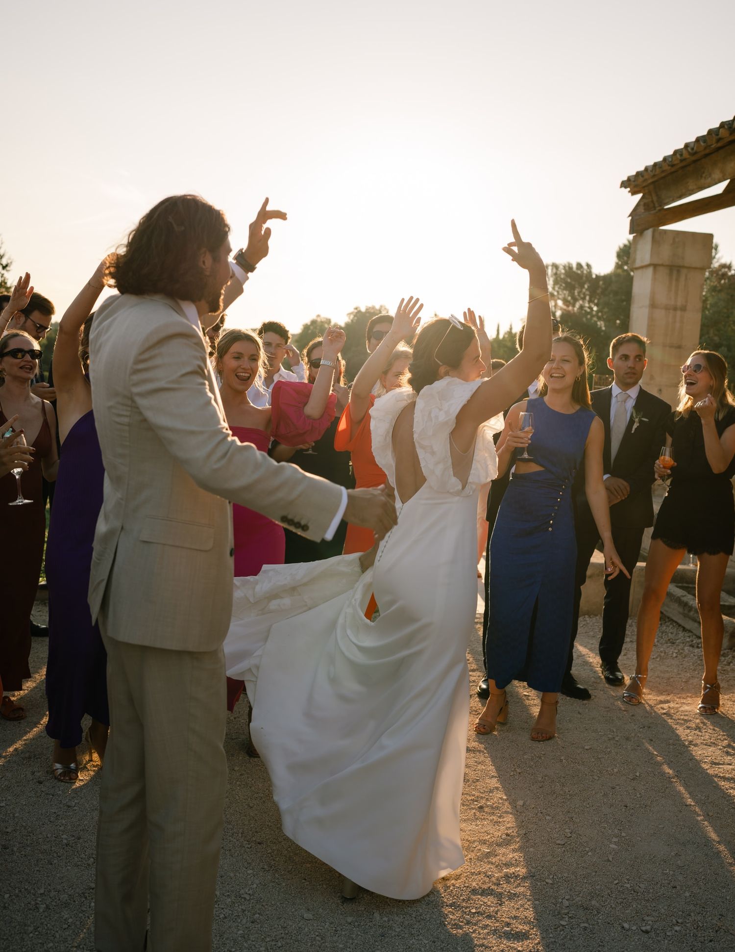 Newlyweds dancing with guests at sunset during outdoor wedding celebration.