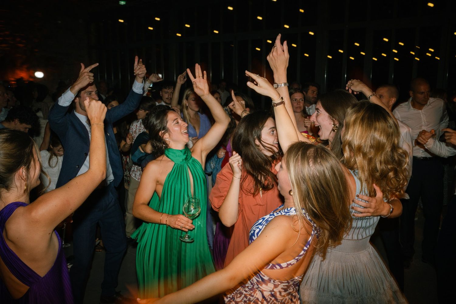 Crowded dance floor filled with celebratory guests dancing with hands raised in the air.