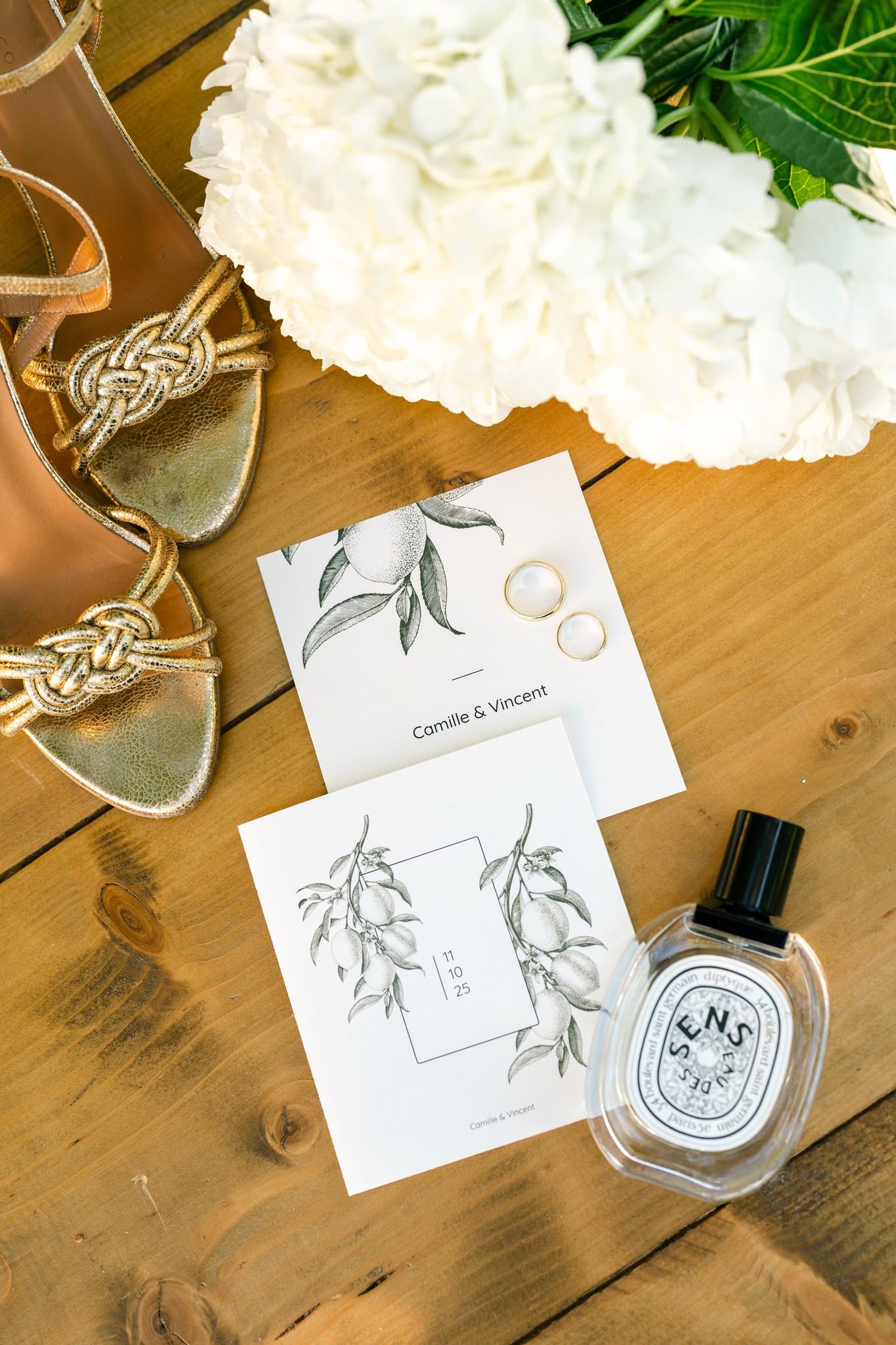 Wedding stationery with olive branch illustrations and white flowers on wooden table.