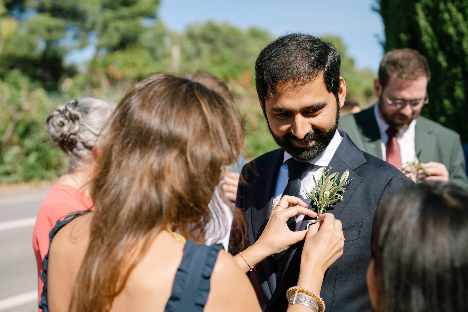 Wedding guests gather outdoors in a garden setting during a sunny celebration.