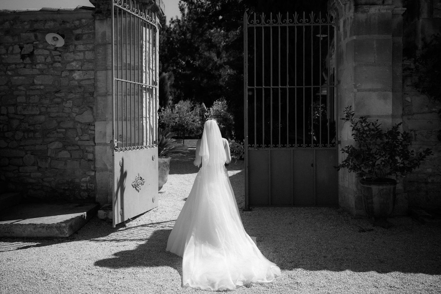 Dramatic silhouette of a bride in her wedding gown against an ornate iron gate and stone wall.