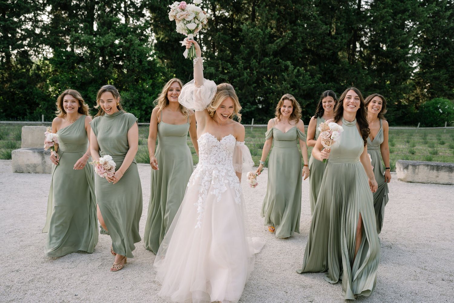Wedding party in sage dresses and white gown walking together on a garden path.