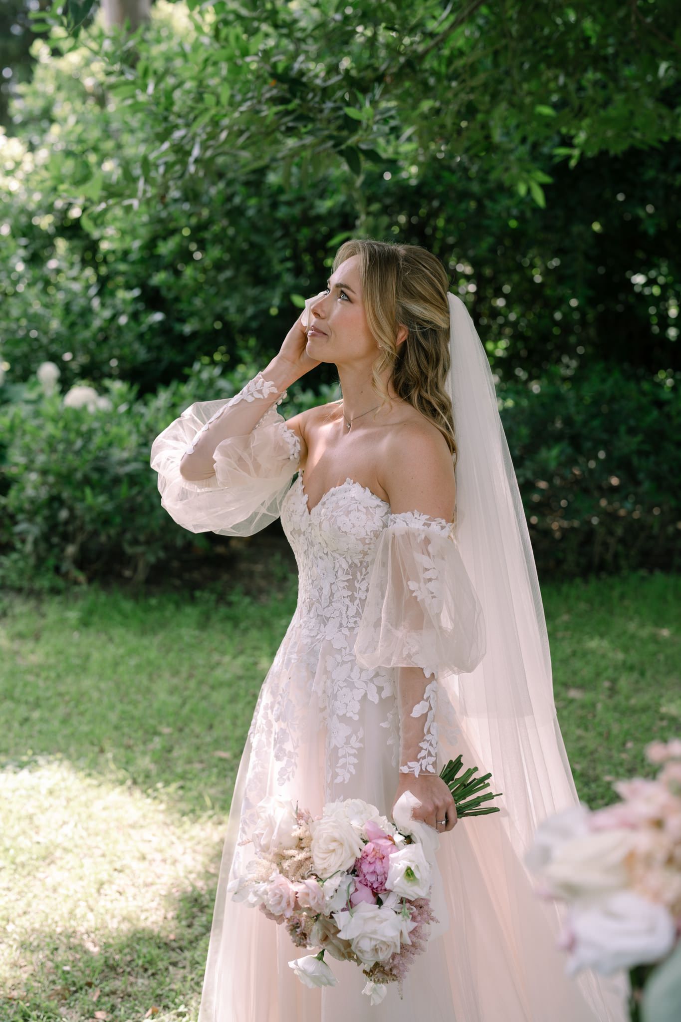 Ethereal bridal portrait in a garden setting featuring a romantic off-shoulder wedding gown.