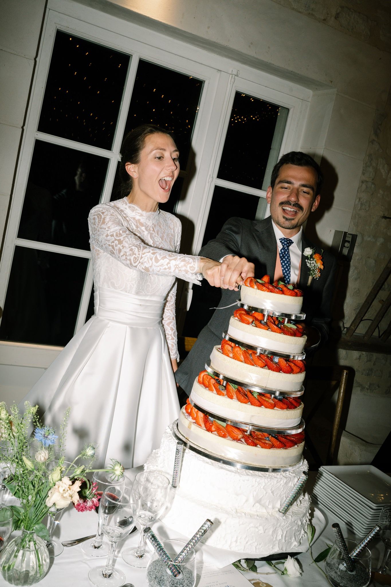 A white tiered wedding cake with orange floral decorations sits on an elegant table setting.