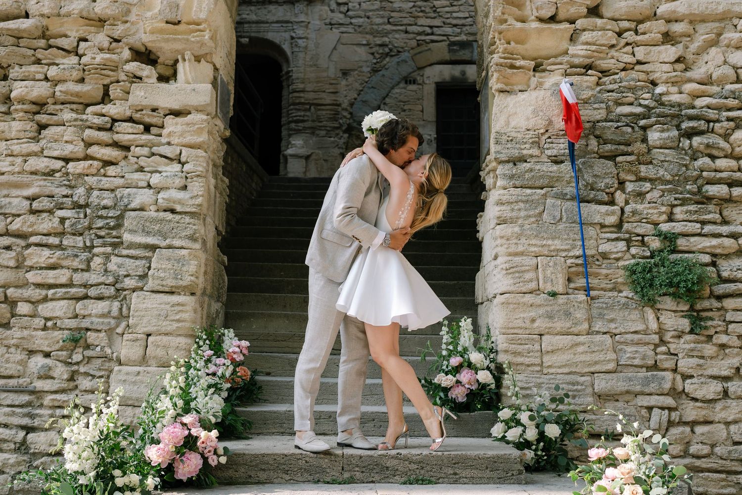 Stone wall backdrop decorated with pink floral arrangements for wedding ceremony.