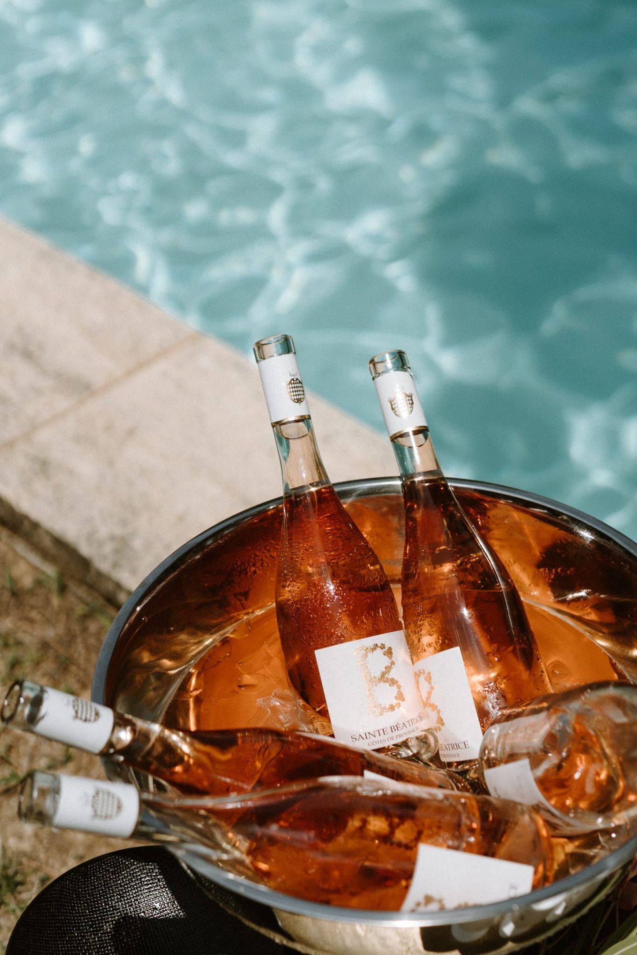 Ice bucket filled with chilled bottles in amber tones against turquoise water background.