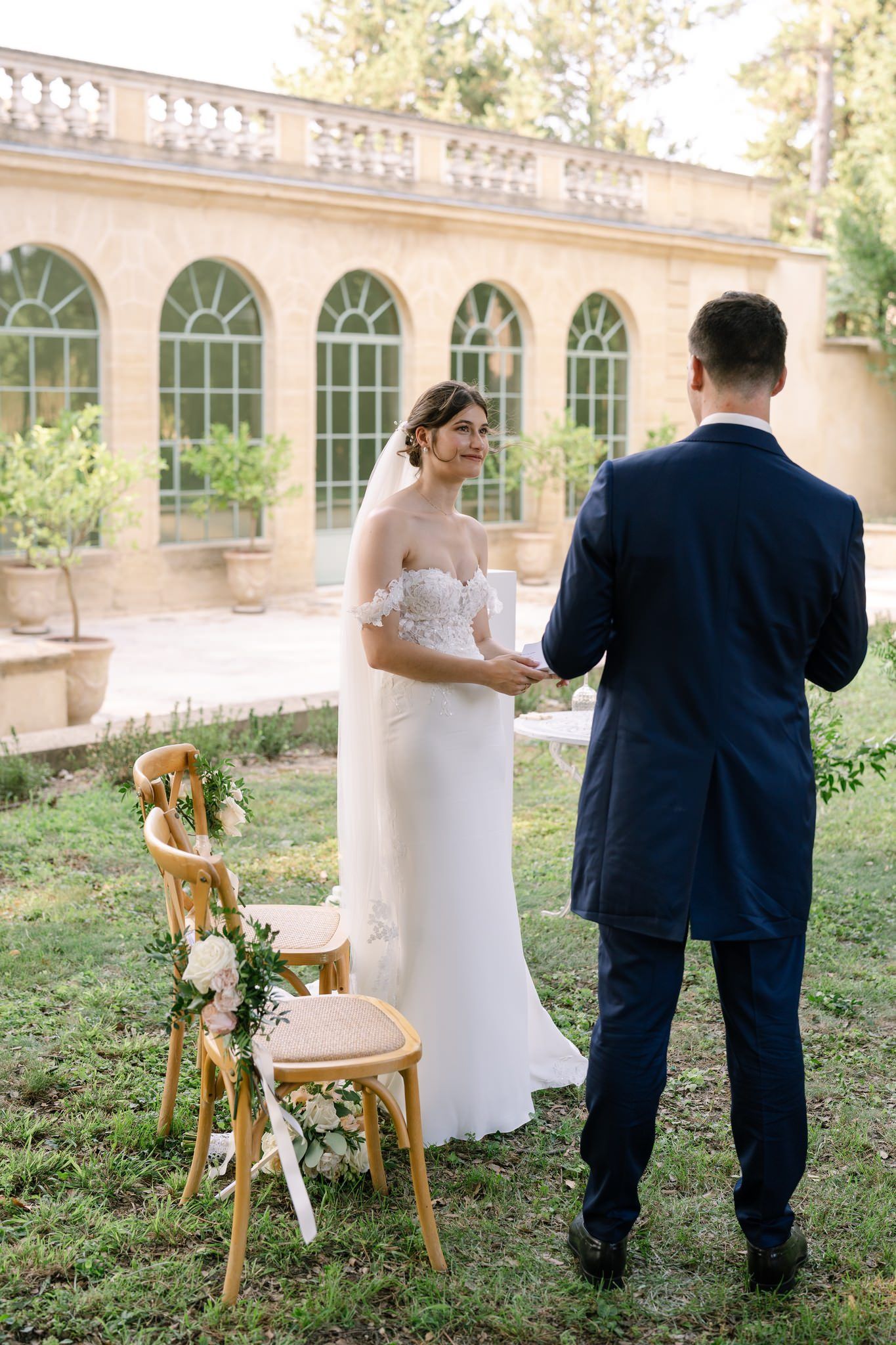 Wedding couple poses in garden setting near classical architecture.