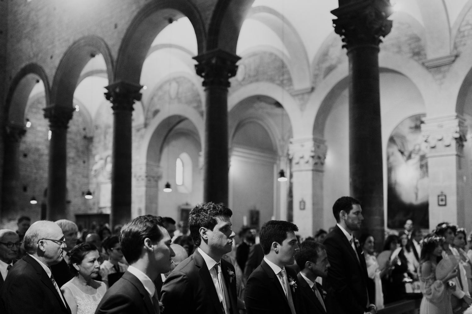 Black and white photo of wedding guests gathered in historic church with arched columns.