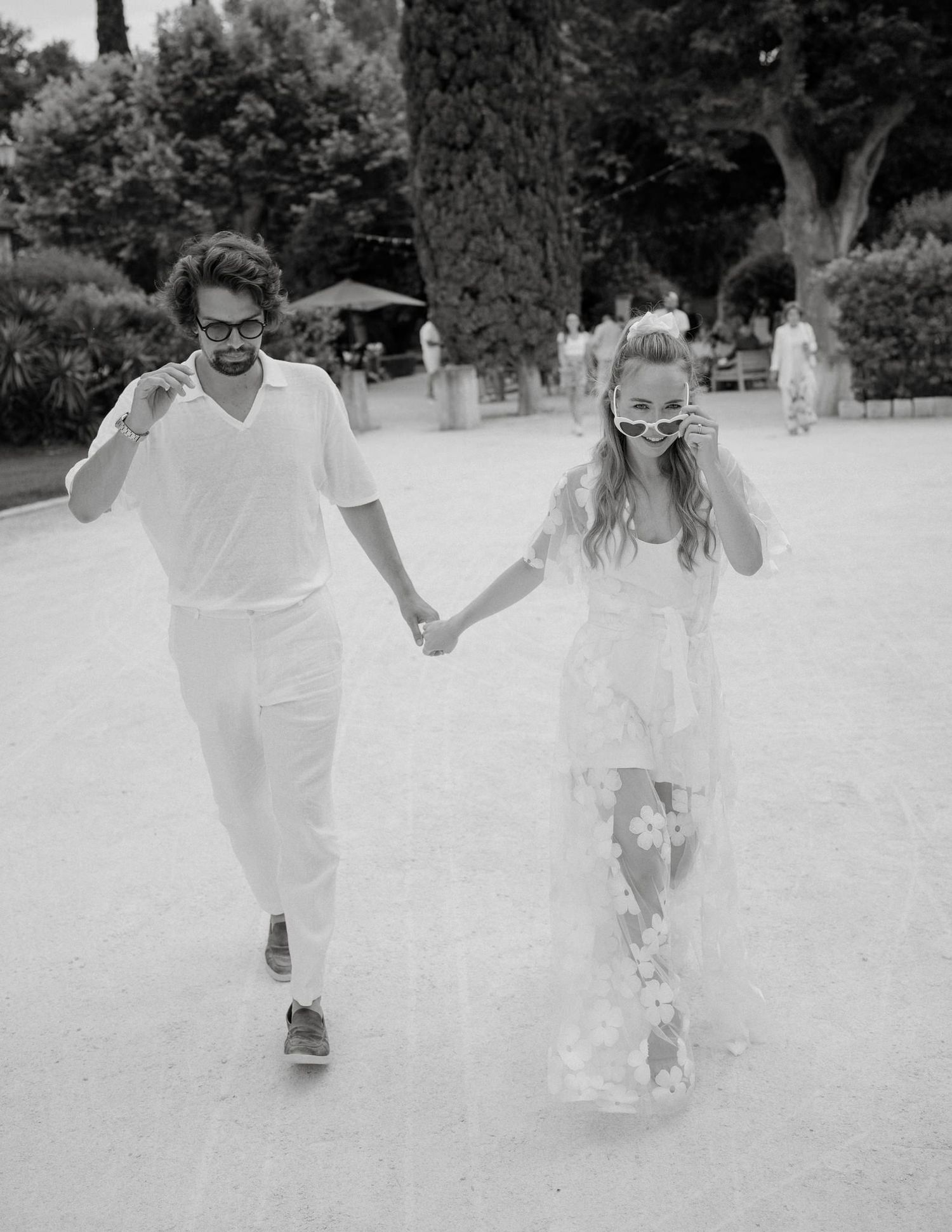 Black and white photo of a couple walking hand in hand while wearing matching white outfits.