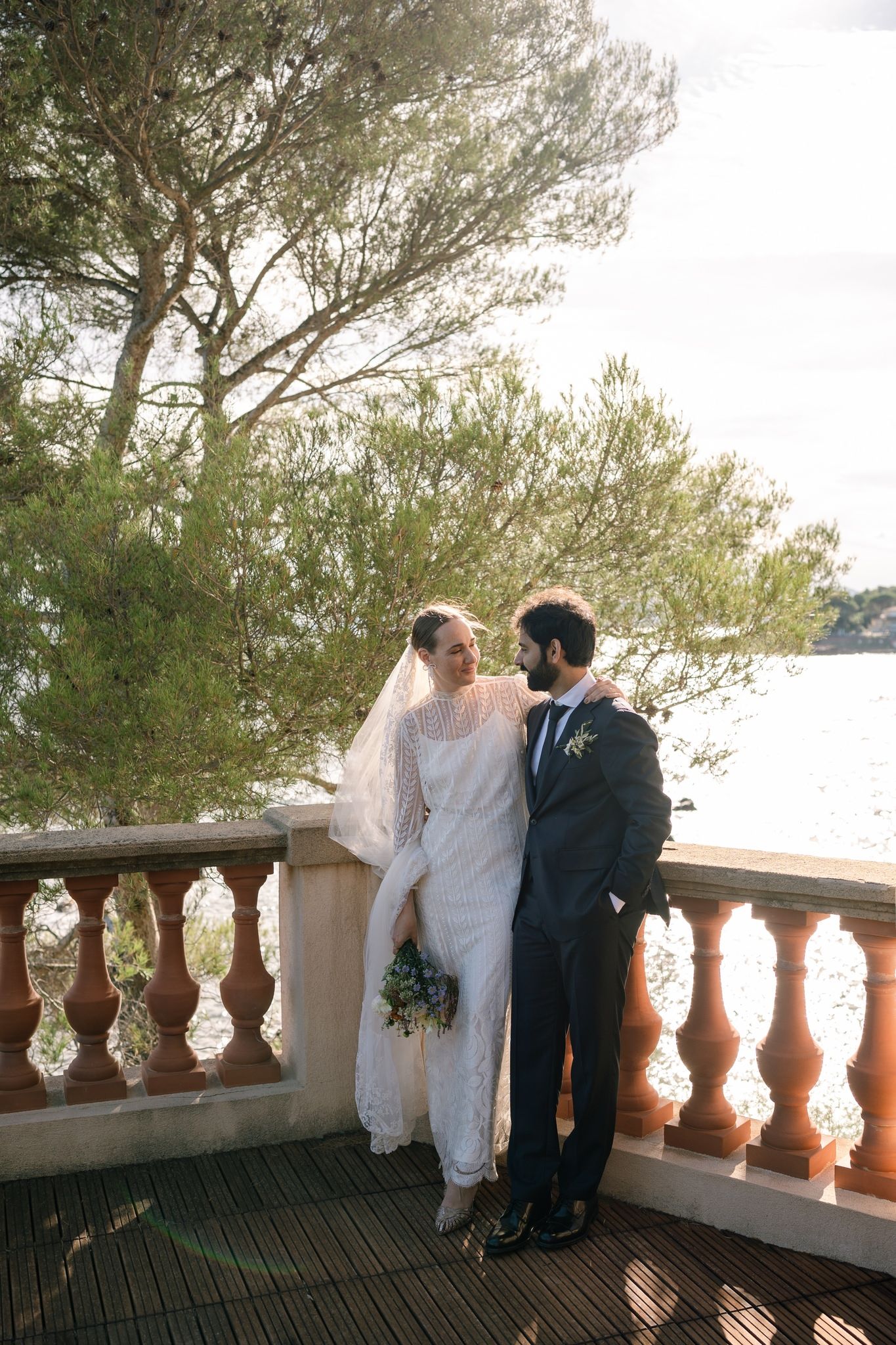 Newlyweds share an intimate moment on a balcony with ornate stone railings.
