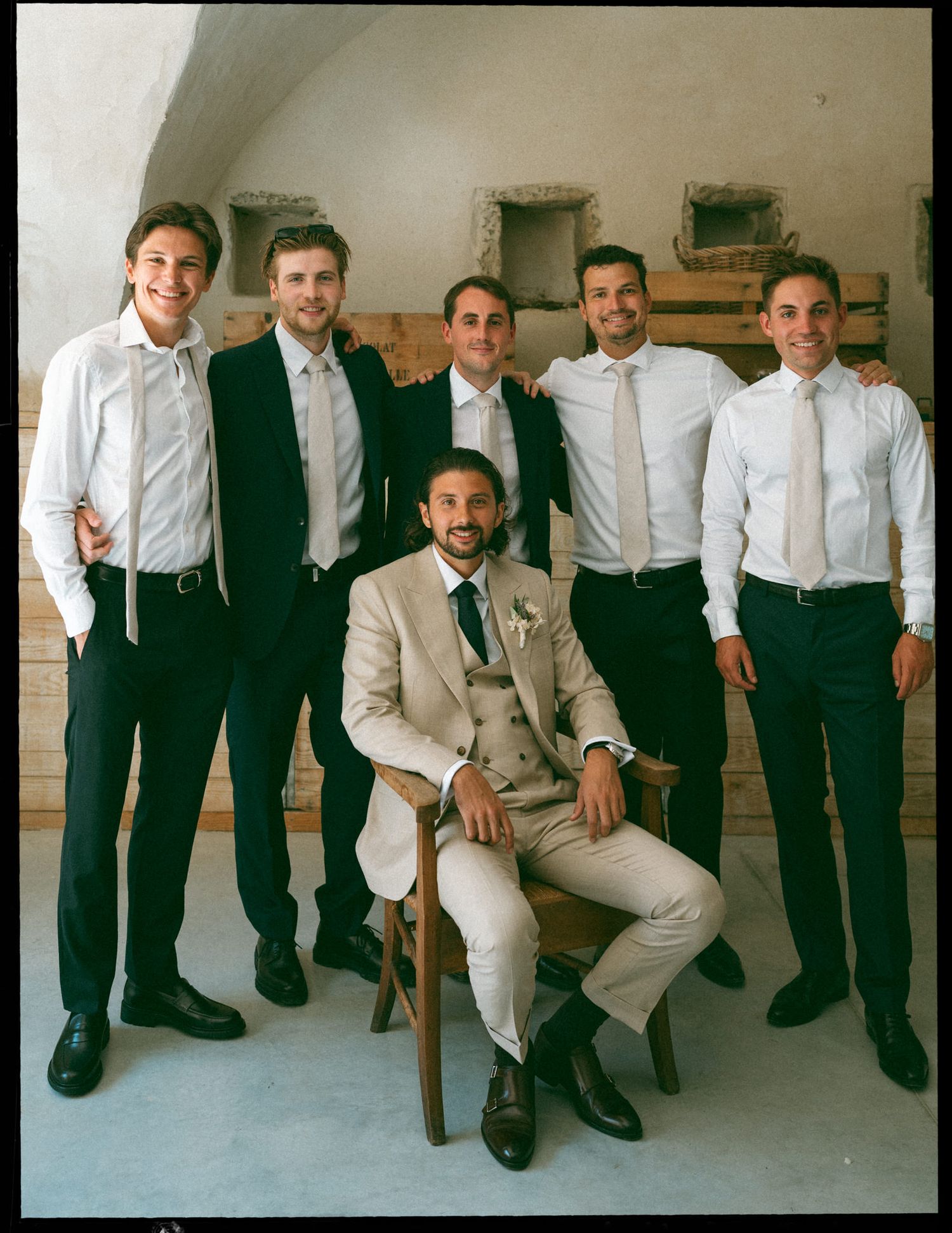 Groomsmen in black and white attire pose casually with one seated member in a light colored suit.