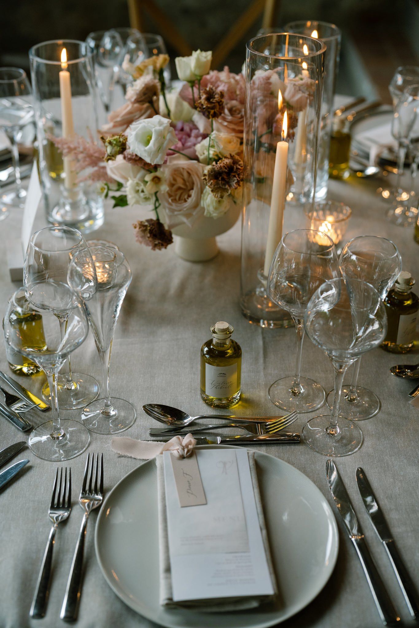 Intimate table setting with blush floral centerpiece, tall candles, and crystal glassware on linen tablecloth.
