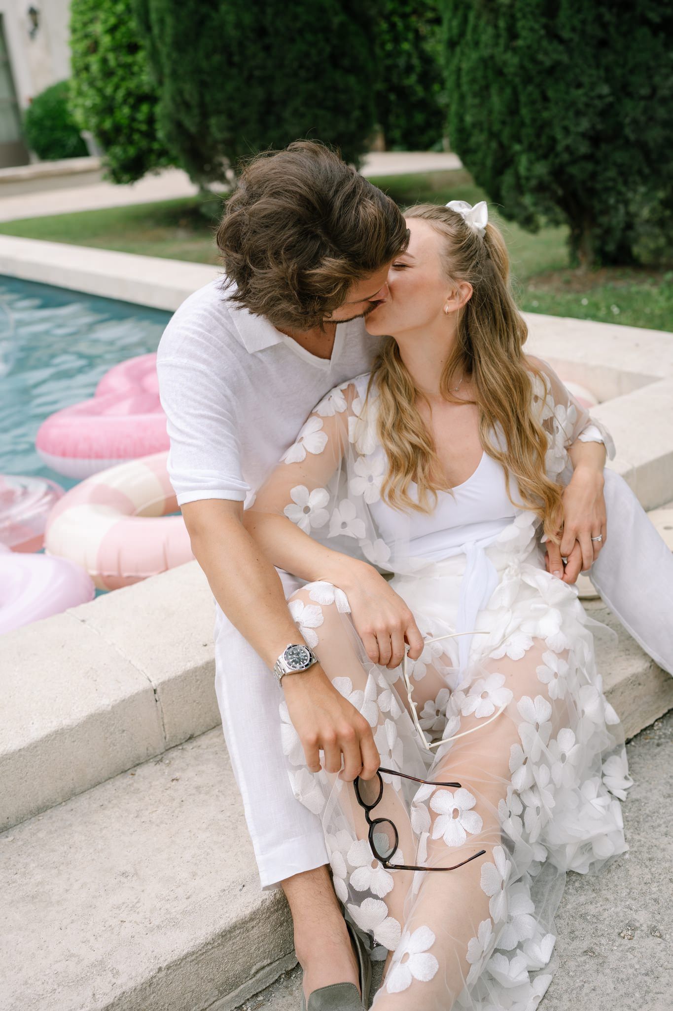 Couple in white outfits relaxing by a pool with decorative floral details.