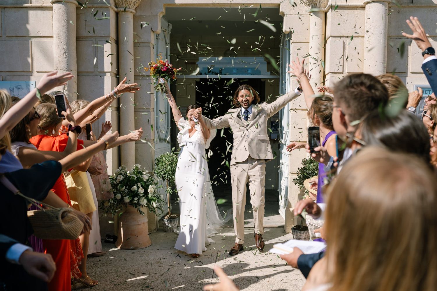 Wedding guests tossing confetti outside church as newlyweds celebrate.