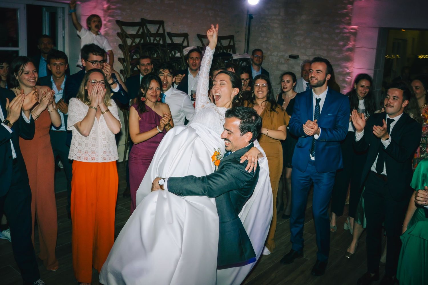 Wedding reception dance party with colorful lighting and energetic crowd.