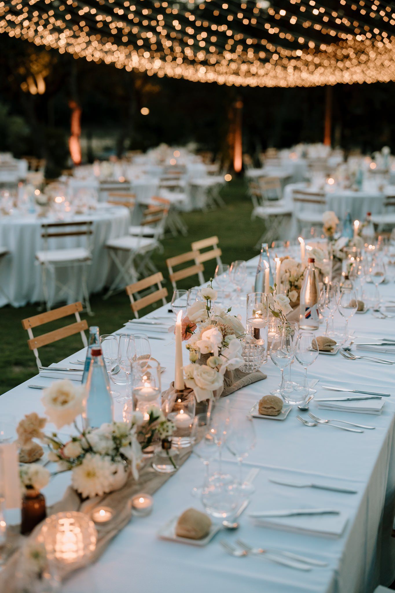 Elegant outdoor wedding reception tables with string lights and floral centerpieces.