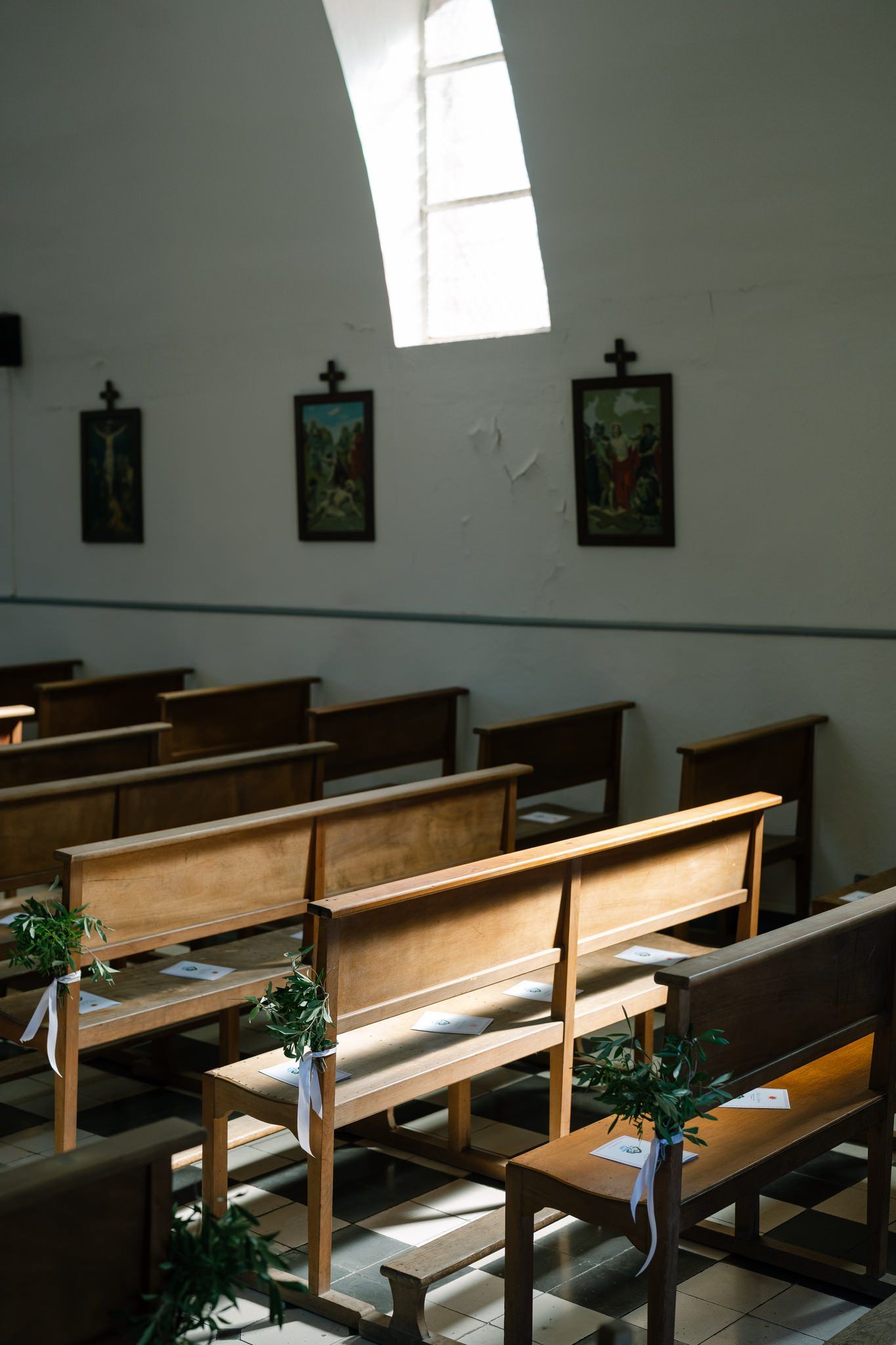 Sunlight streams through windows into an empty chapel with wooden pews and religious artwork.