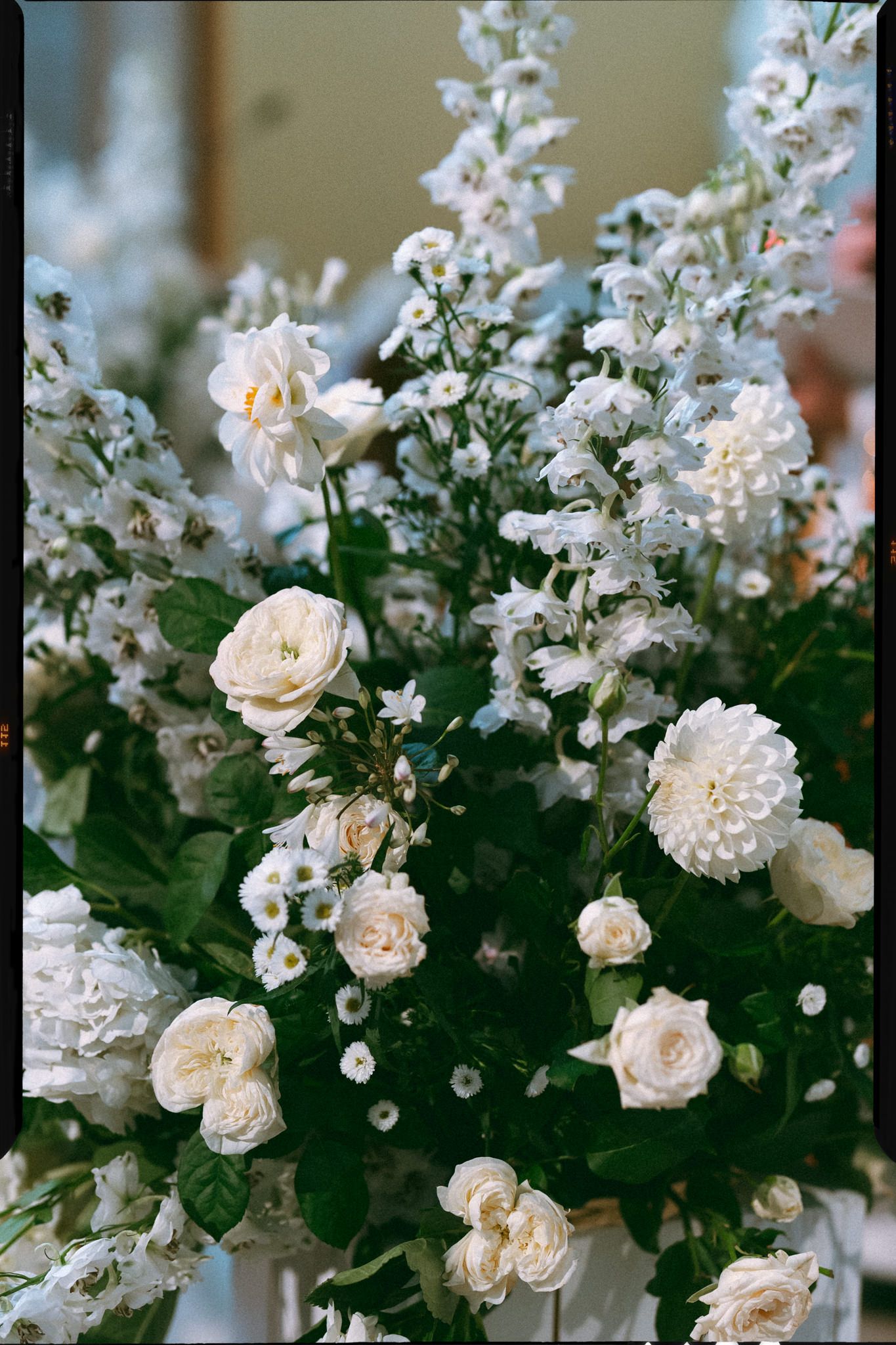 Delicate white roses and small blossoms arranged with lush green foliage in a romantic garden-style floral display.