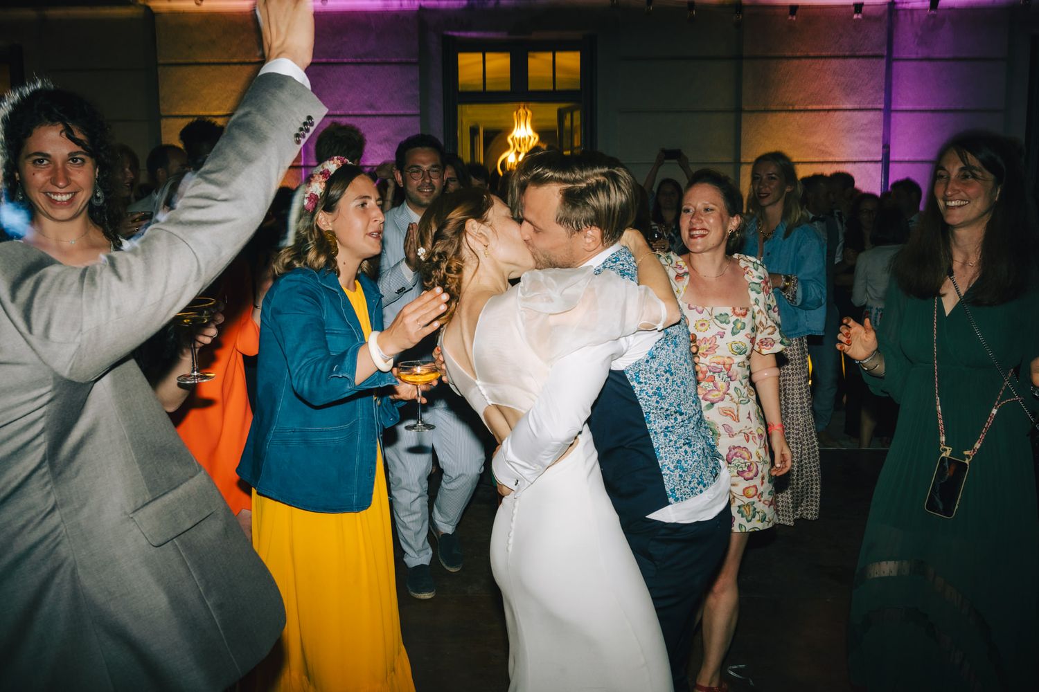 Guests dancing and celebrating at a wedding reception with vibrant purple lighting.