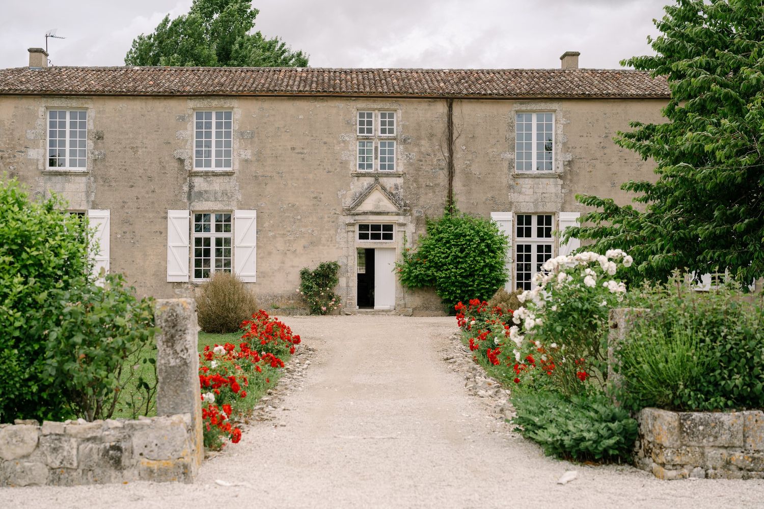 Exterior view of a traditional stone manor house with red flowers in the garden.