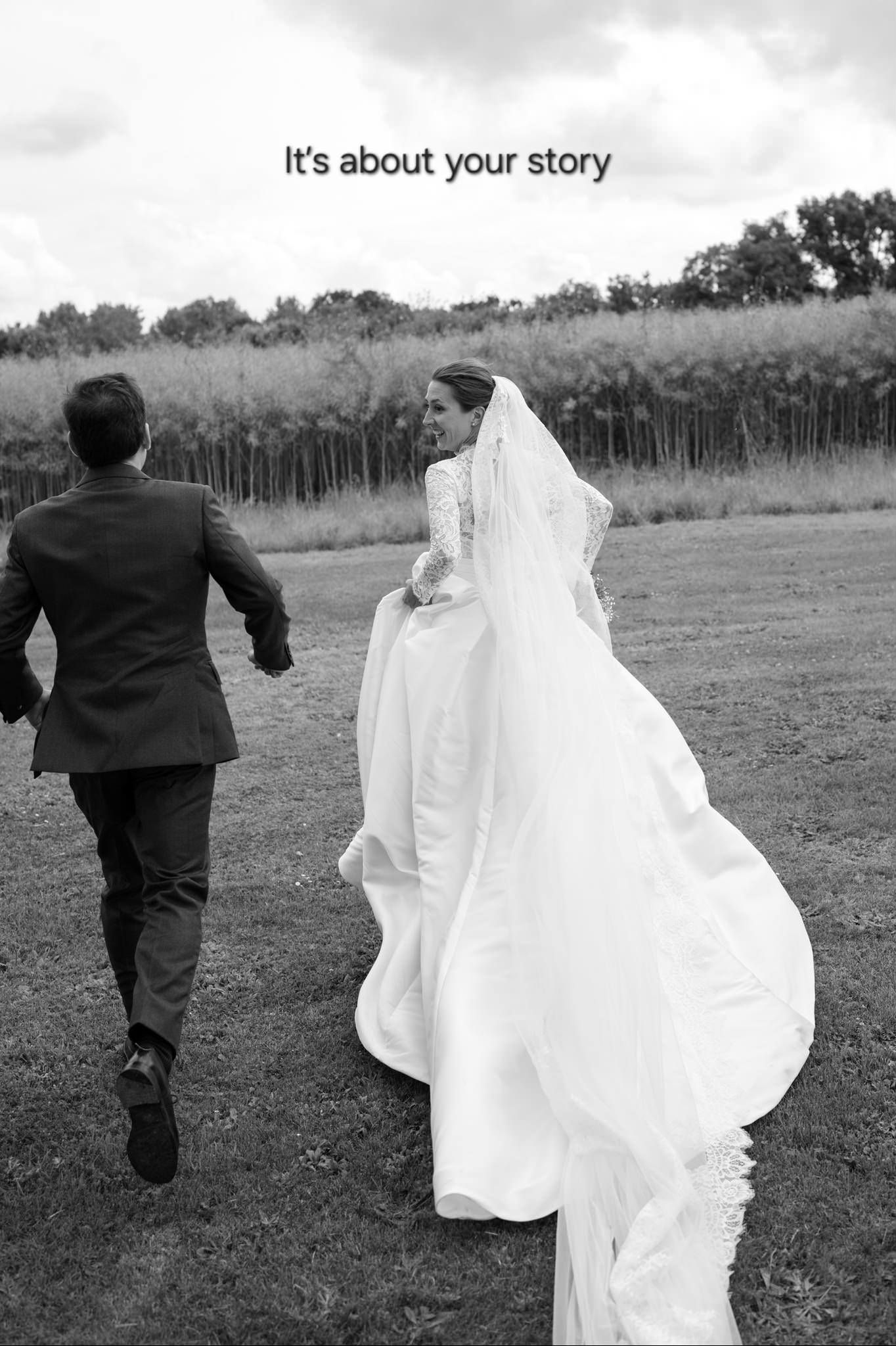 Black and white photo of a bride and groom running through a field with her flowing white dress and veil trailing behind.