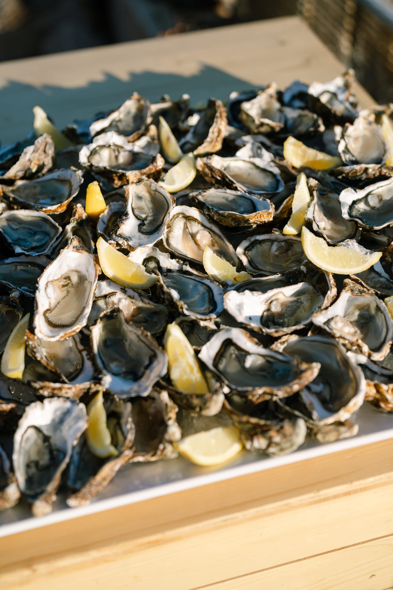 Fresh oysters on the half shell served with lemon wedges on a wooden surface.