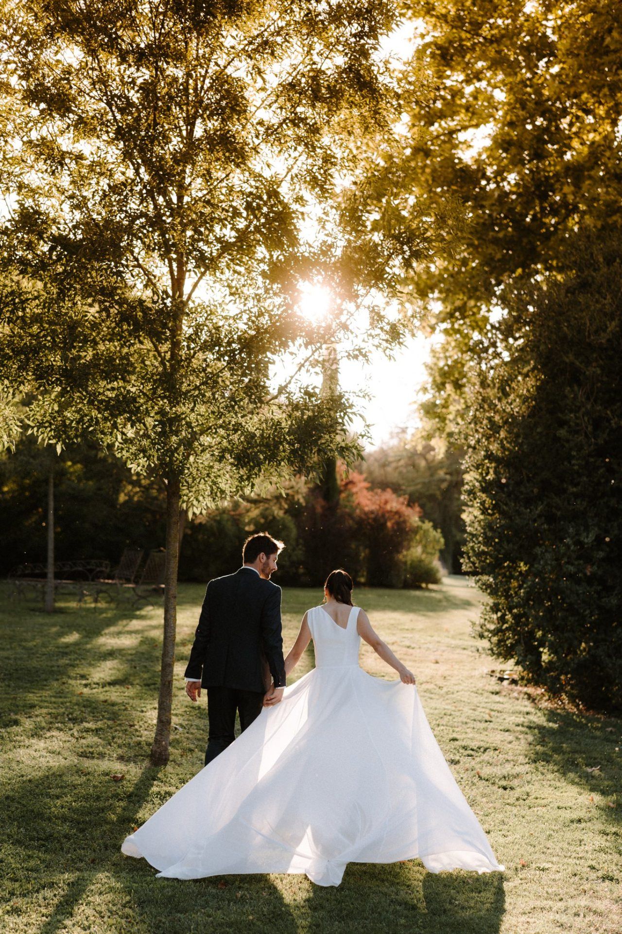 Wedding couple walking through a sunlit park with golden autumn trees.
