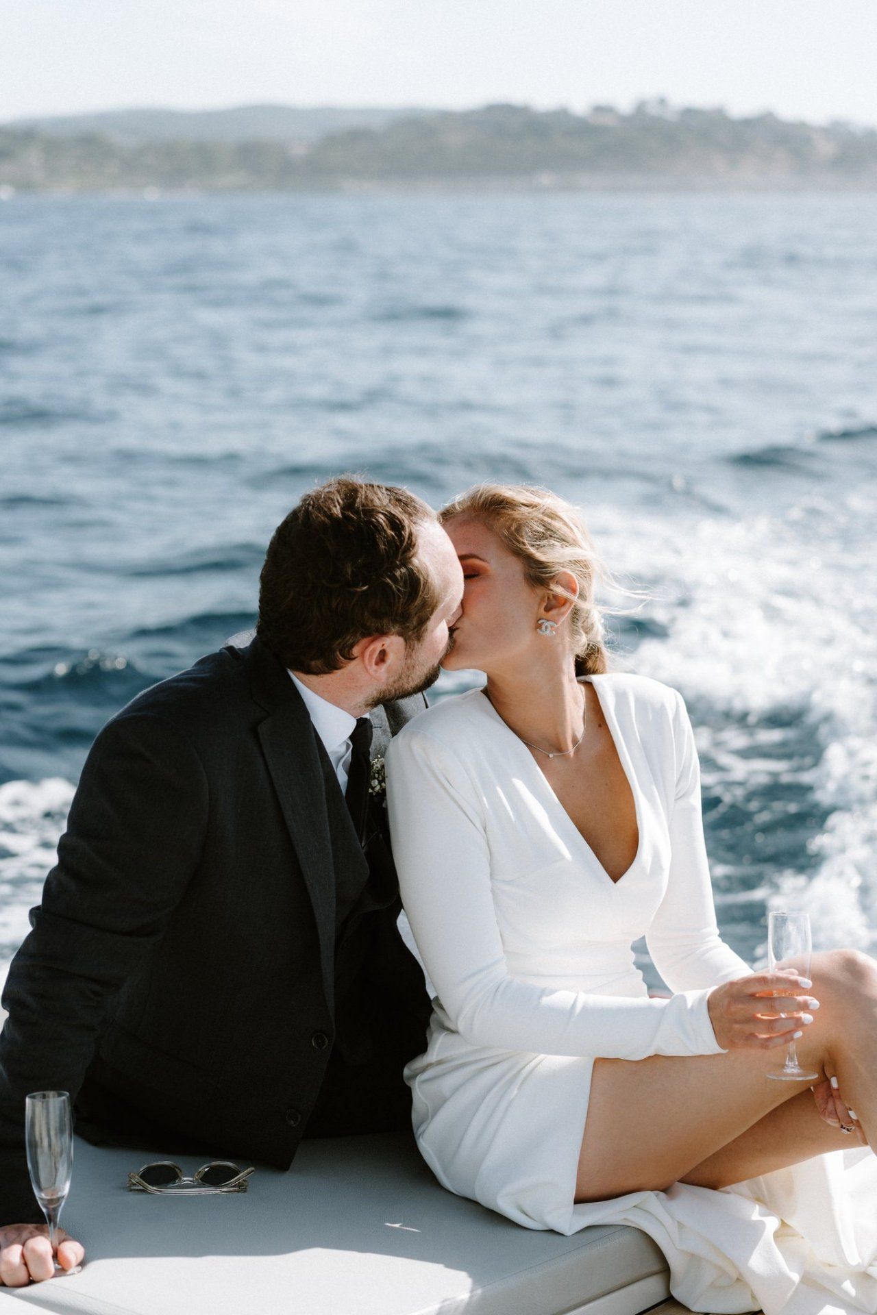 Romantic couple in wedding attire sharing intimate moments on a boat with ocean waves in background.
