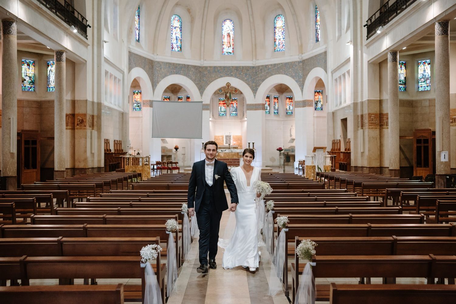 A beautiful church interior with white walls, arched windows, and wooden pews during a wedding ceremony.
