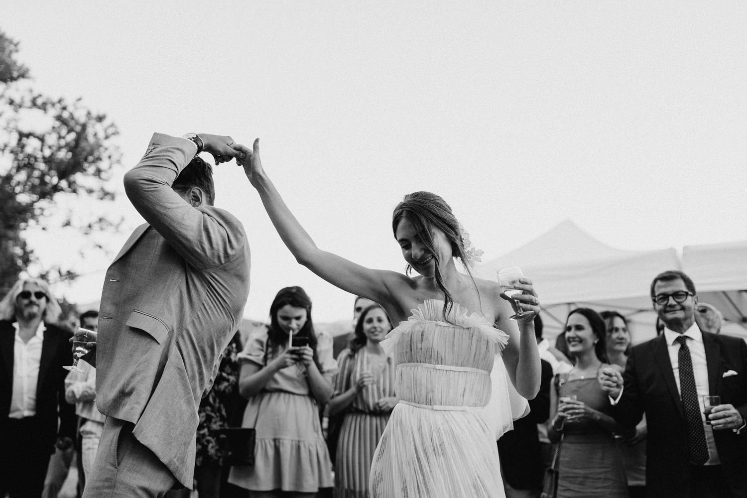 Wedding guests dancing and celebrating under outdoor tent at dusk.