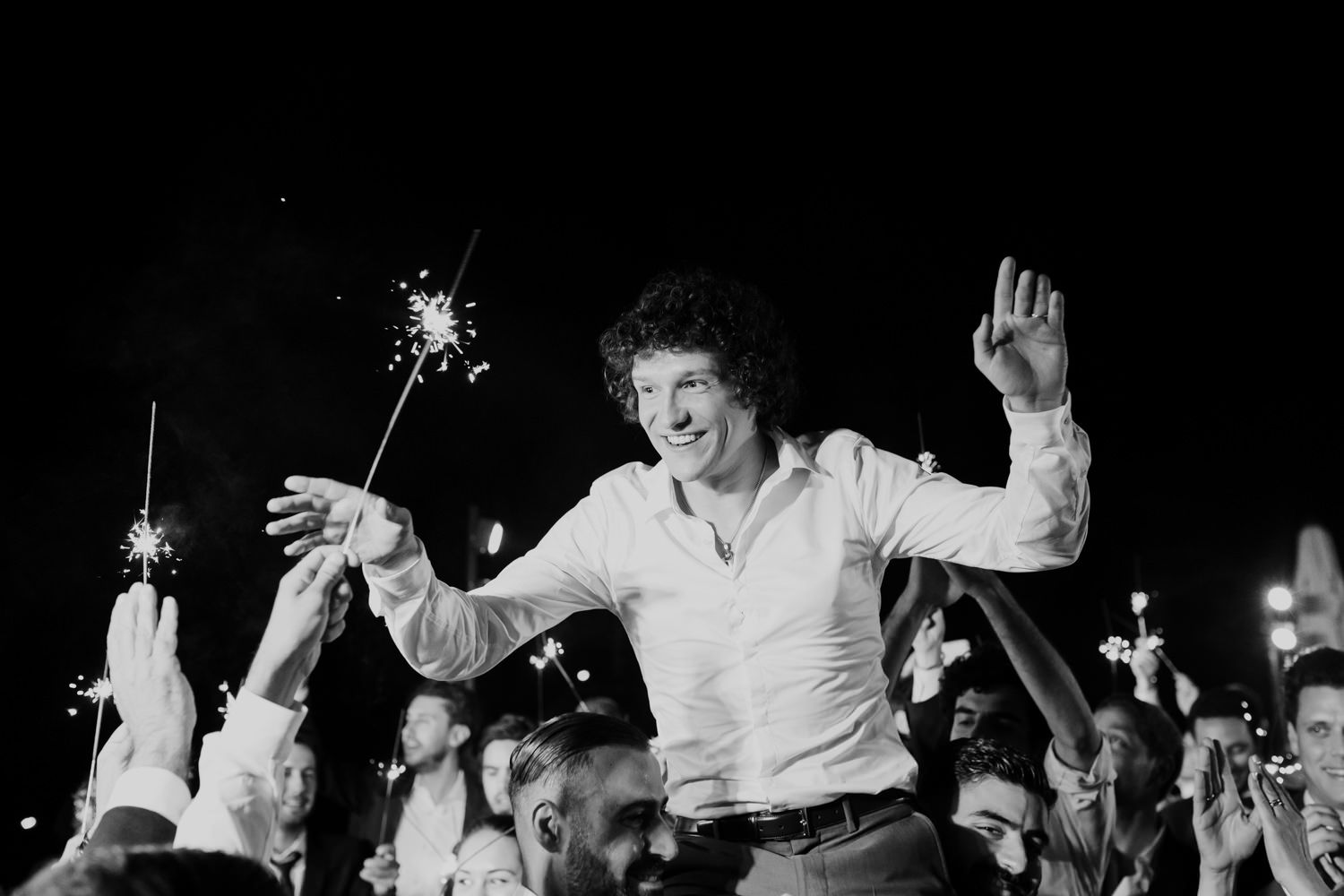 Black and white photo of wedding guests dancing energetically at a nighttime celebration.