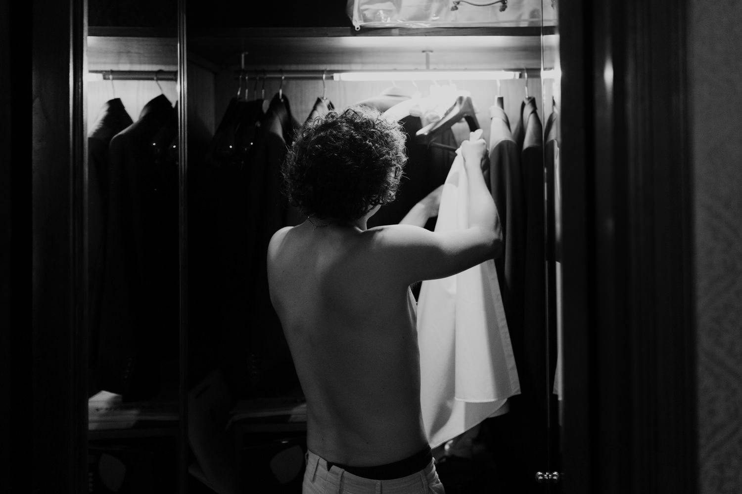 A black and white photo showing someone reaching for a dress in a closet.